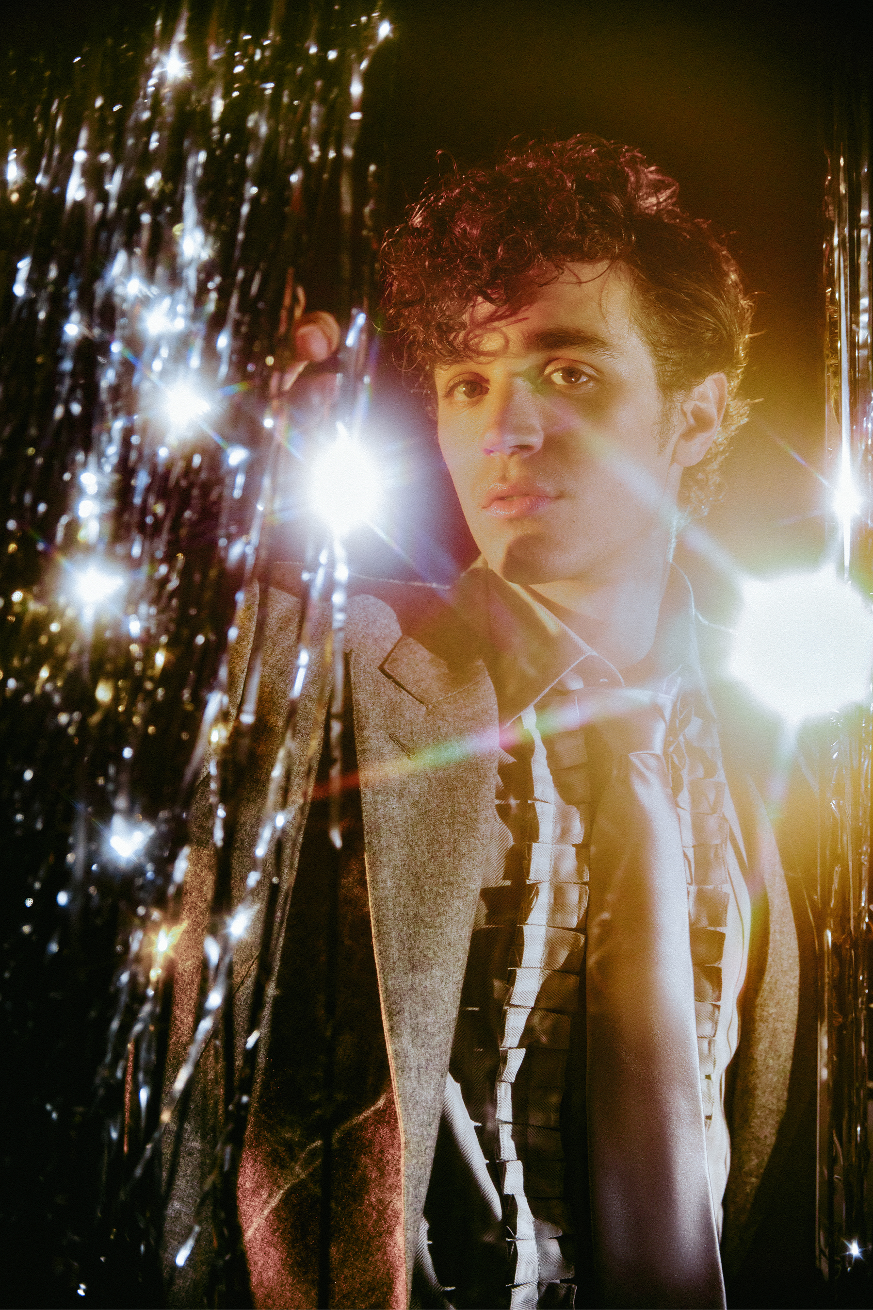 Fear Street: Prom Queen actor David Iacono with a silver tinsel backdrop wearing a Wolk Morais suit jacket and shirt.