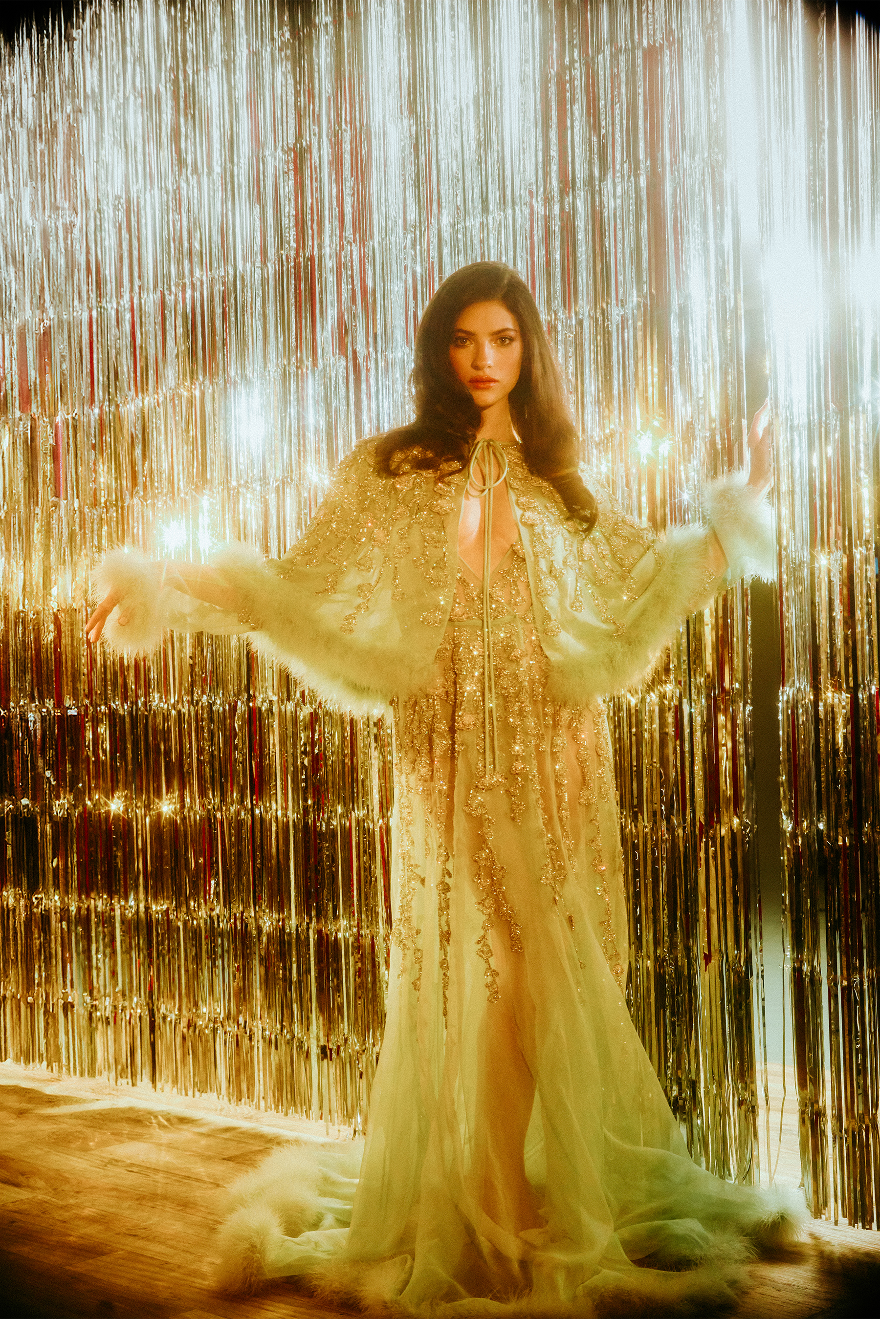 Ella Rubin stands in front of a silver tinsel backdrop wearing a floor-length mint green Valentino gown with jewel embellishments and furry detailing at the hemline and a matching capelet.