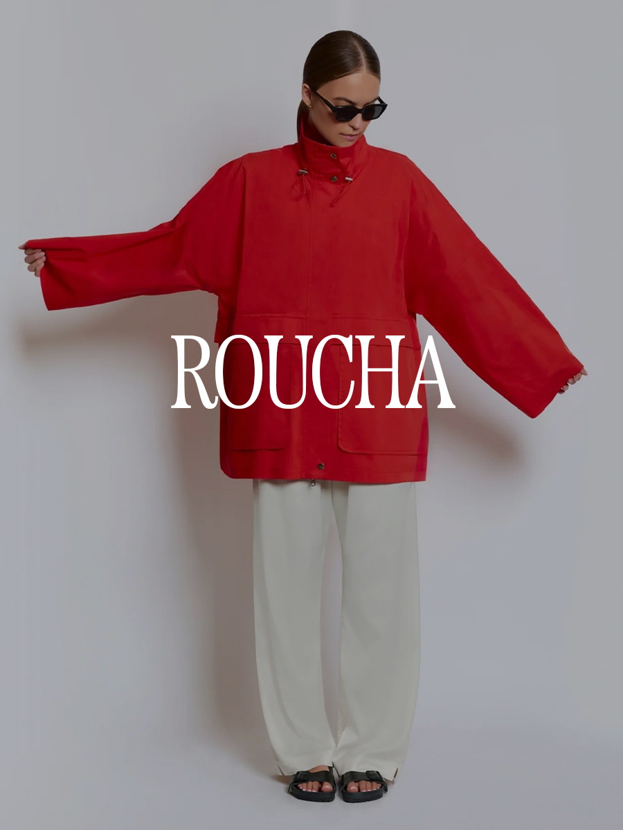 A photo of a model wearing a Roucha red sporty jacket and cream pants. Text says "Roucha" in white capital serif letters.