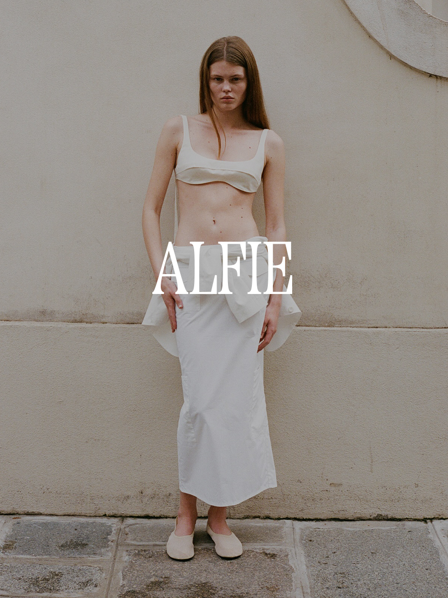 A photo from Alfie's lookbook of a model wearing a bra and white skirt. Text says "Alfie" in white capital serif letters.