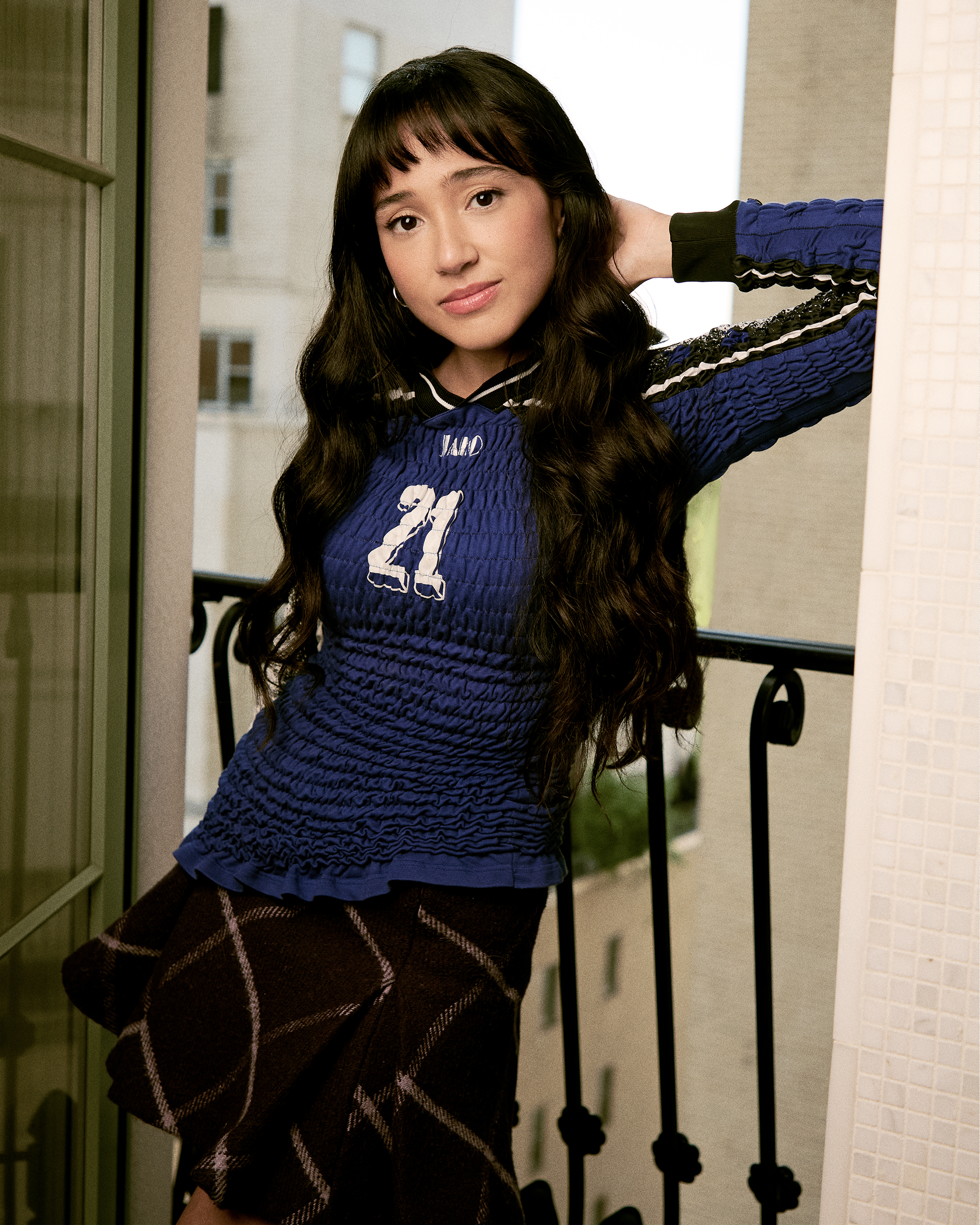 Overcompensating actress Wally Baram poses for portrait at the Plaza Hotel in NYC. She is wearing a long-sleeve smocked blue shirt with the number 21 on the front, a purple plaid miniskirt and black leather boots.