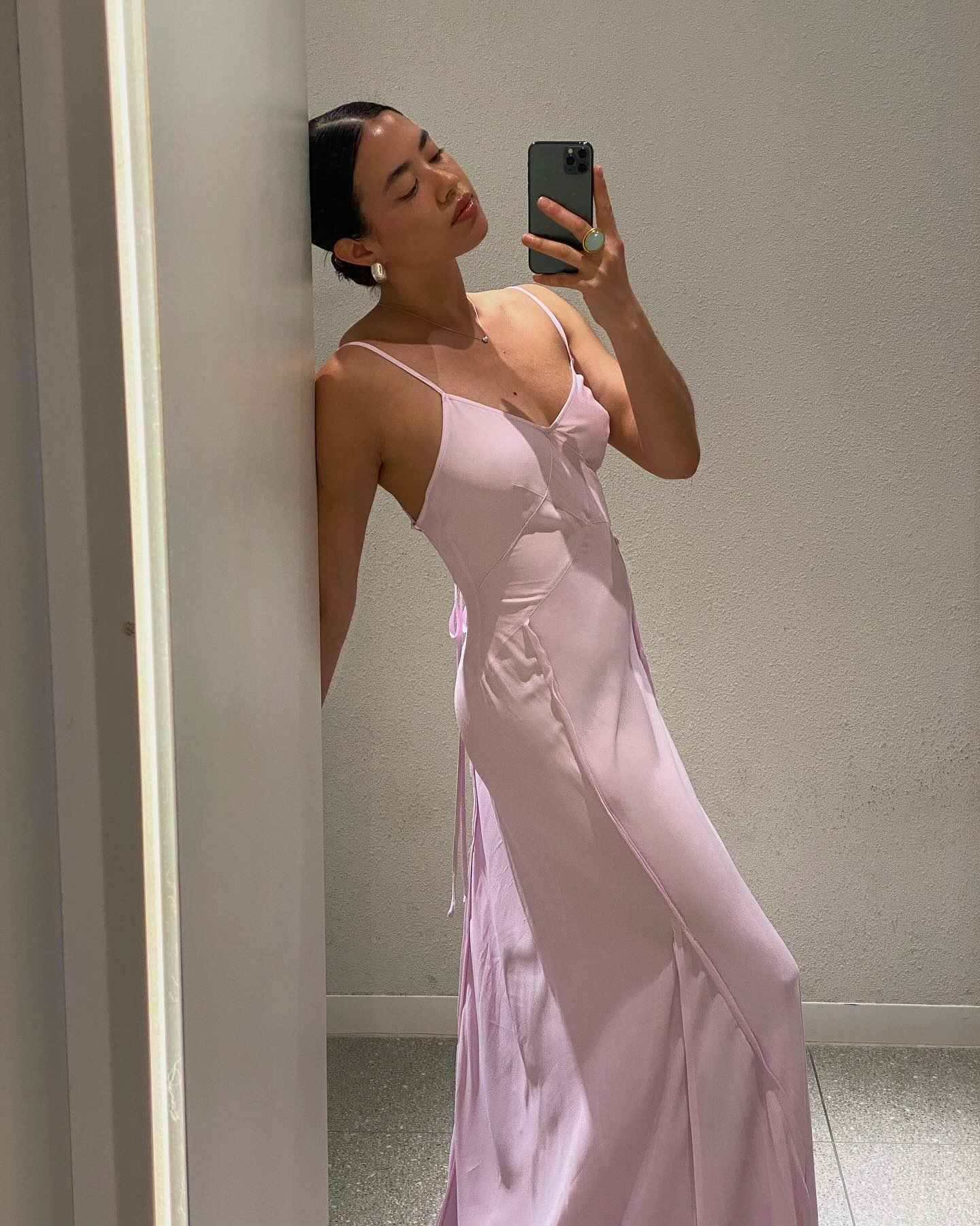 Sasha Mai wears the light pink dress trend. She is wearing a long pale pink dress, silver hoops and is posed in front of a white wall. This image was taken from her Instagram recently.