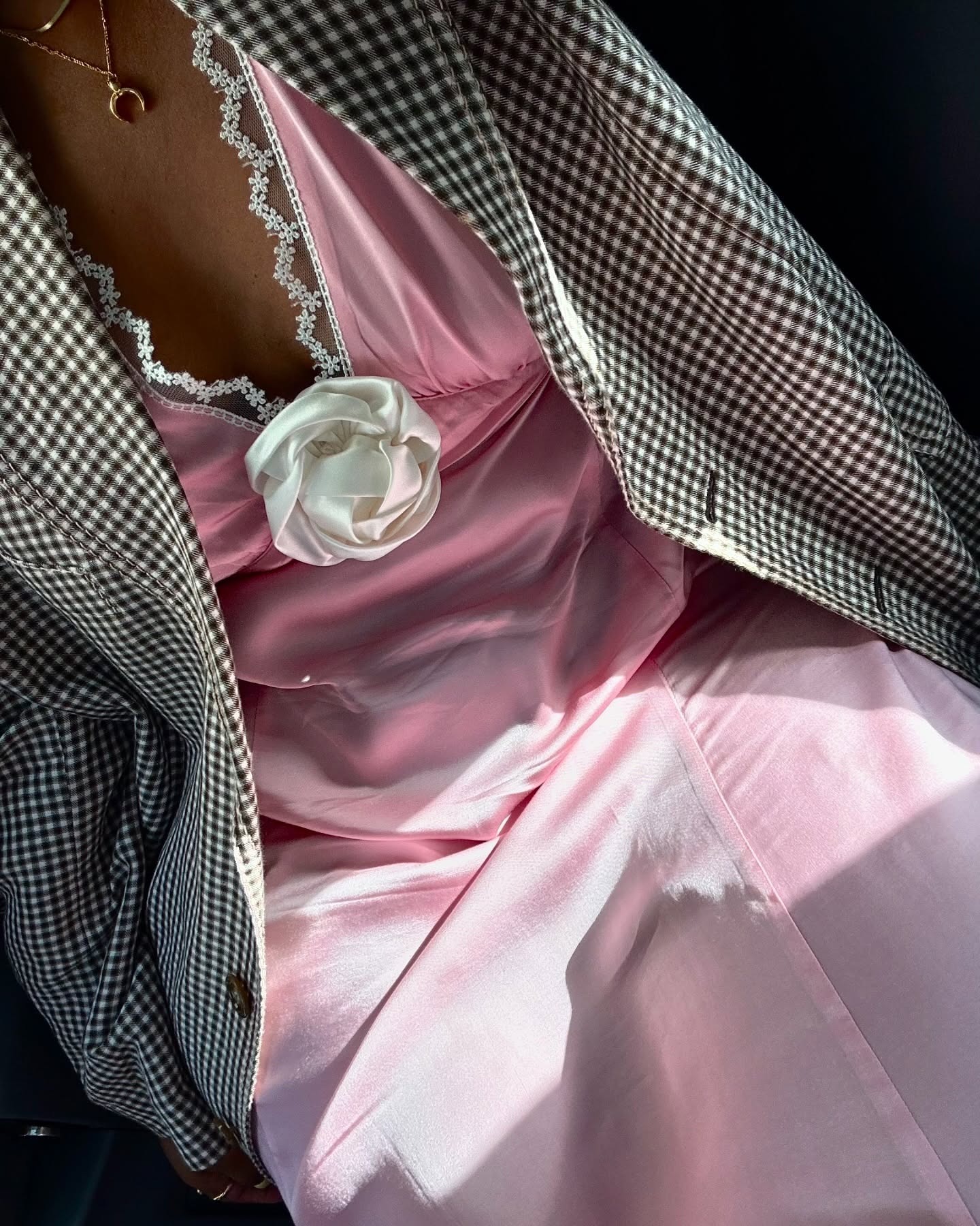 Stylist Karina Marriot wears a light pink silk-like dress with white lace detailing and a large white rose. She has paired her dress with a black and white checked blazer in a image taken from her Instagram recently.