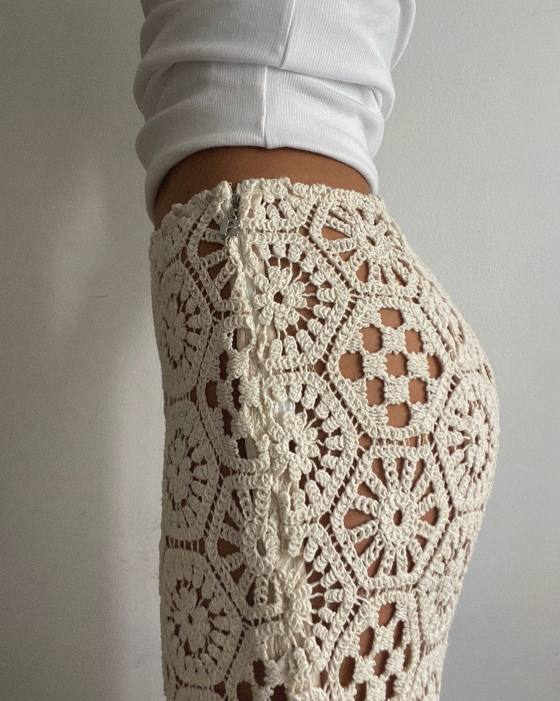 Style influencer Debora Rosa poses for a cropped outfit photo with a white top and beige crochet pants.