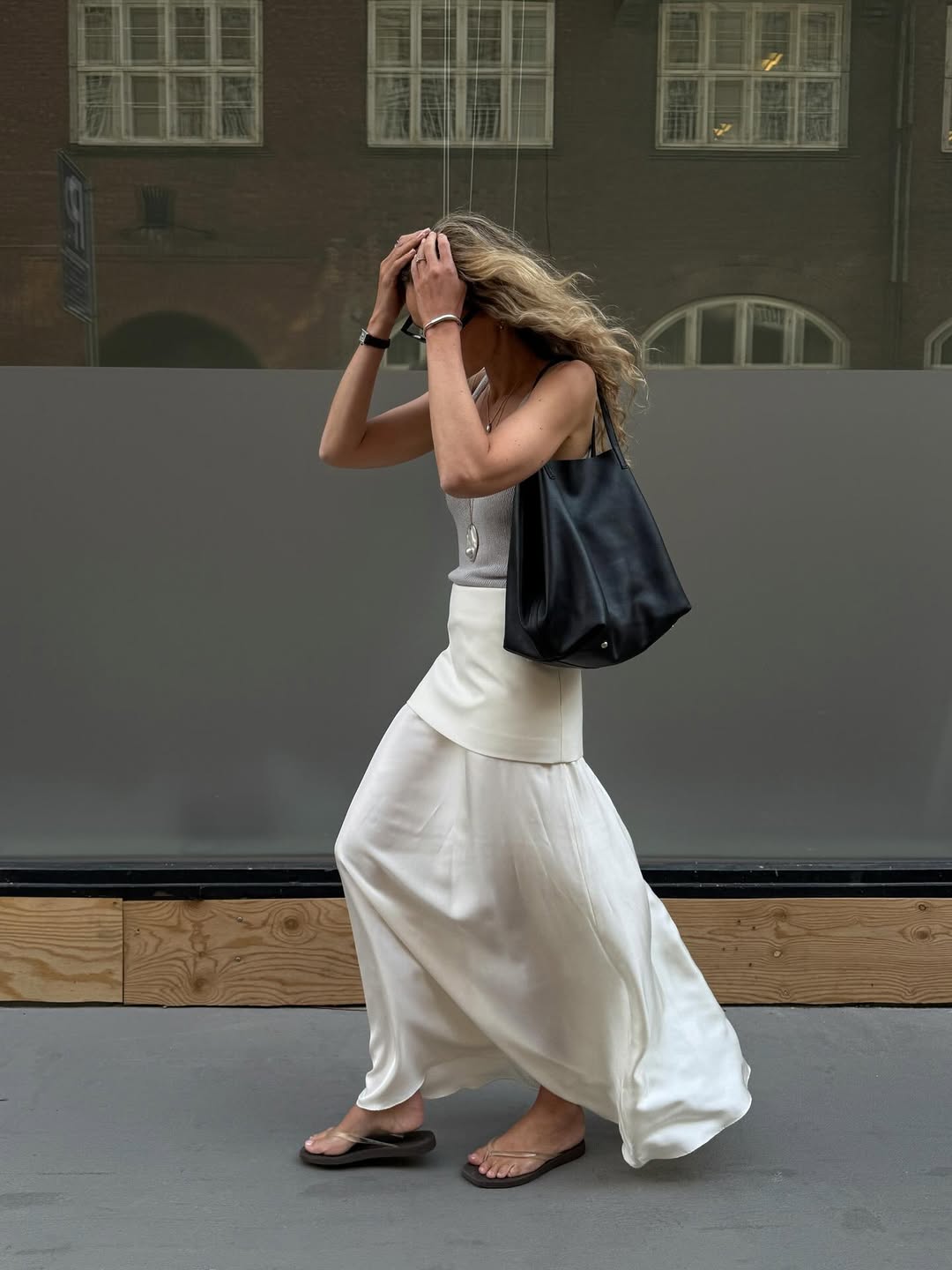 @anoukyve wears clear jelly flip-flops with a grey tank, white maxi skirt and black leather bag
