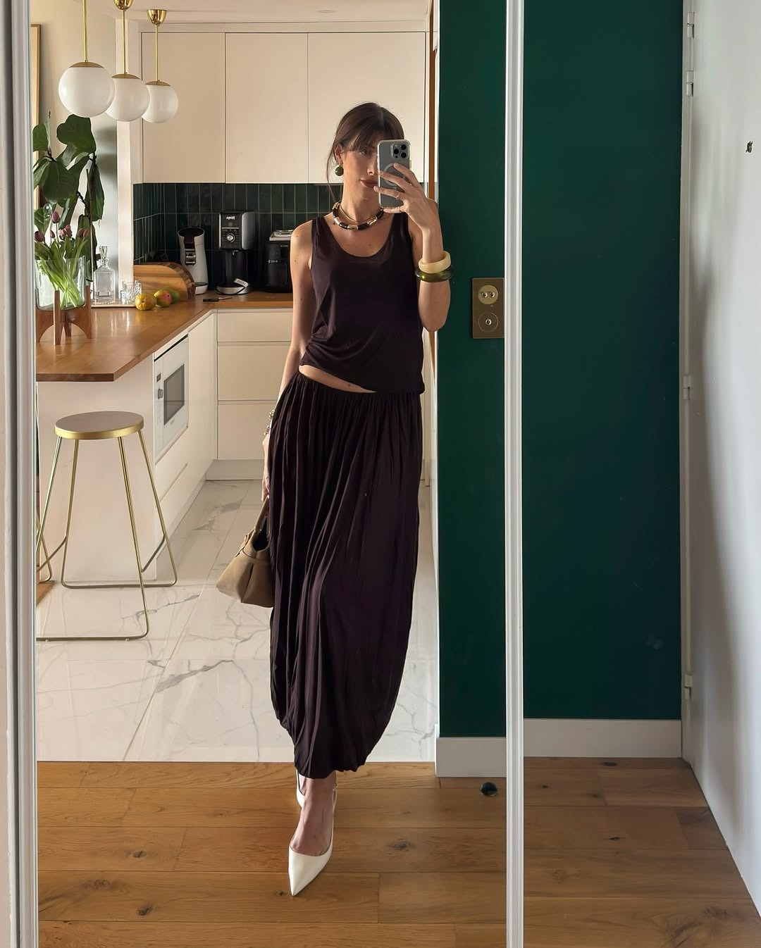A woman standing in front of a mirror wearing a brown puff skirt, a brown t-shirt, and a pair of white pointed-toe heels.
