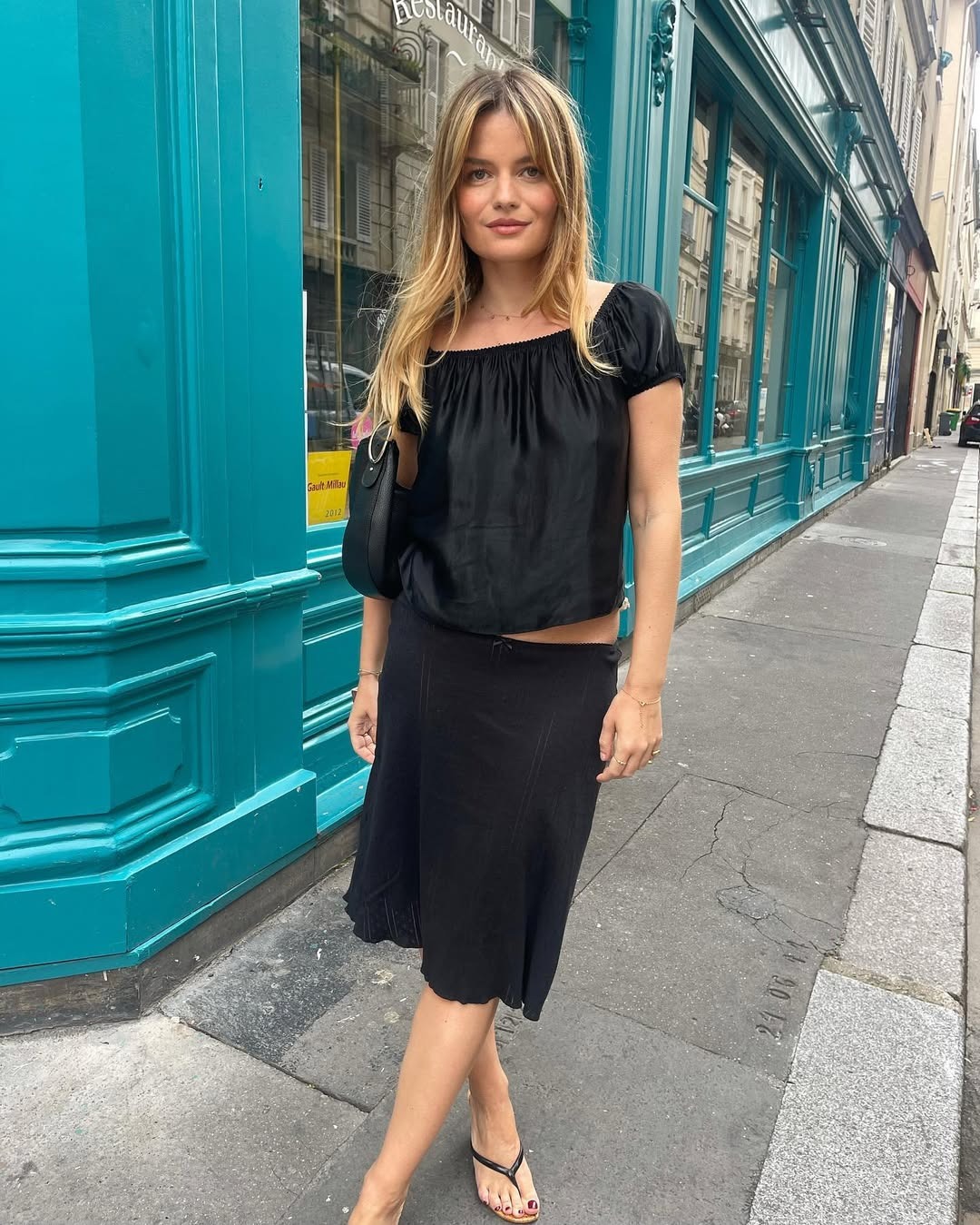 A woman standing wearing a black slip skirt and a black peasant style top.