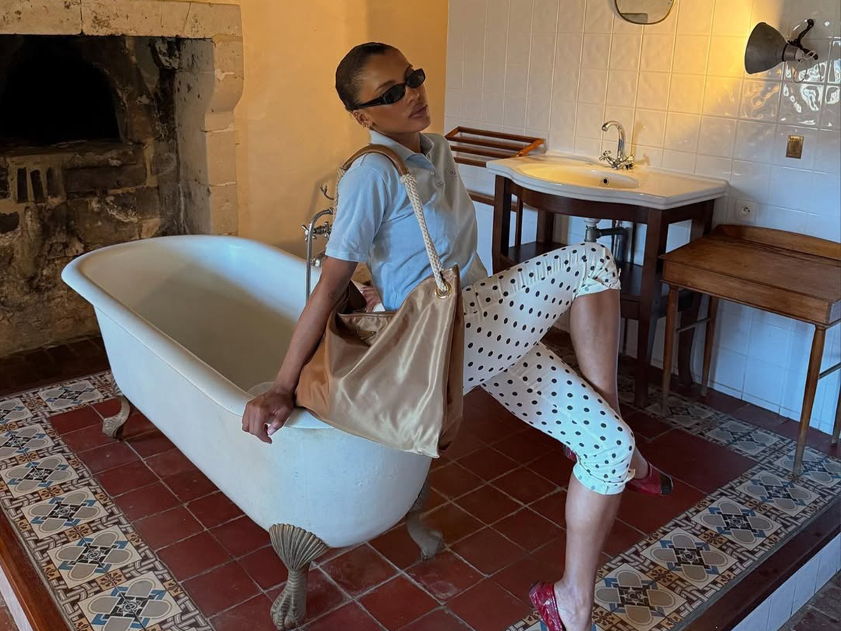 A woman sitting wearing polka dot capris, a gray polo, and a large gold tote.