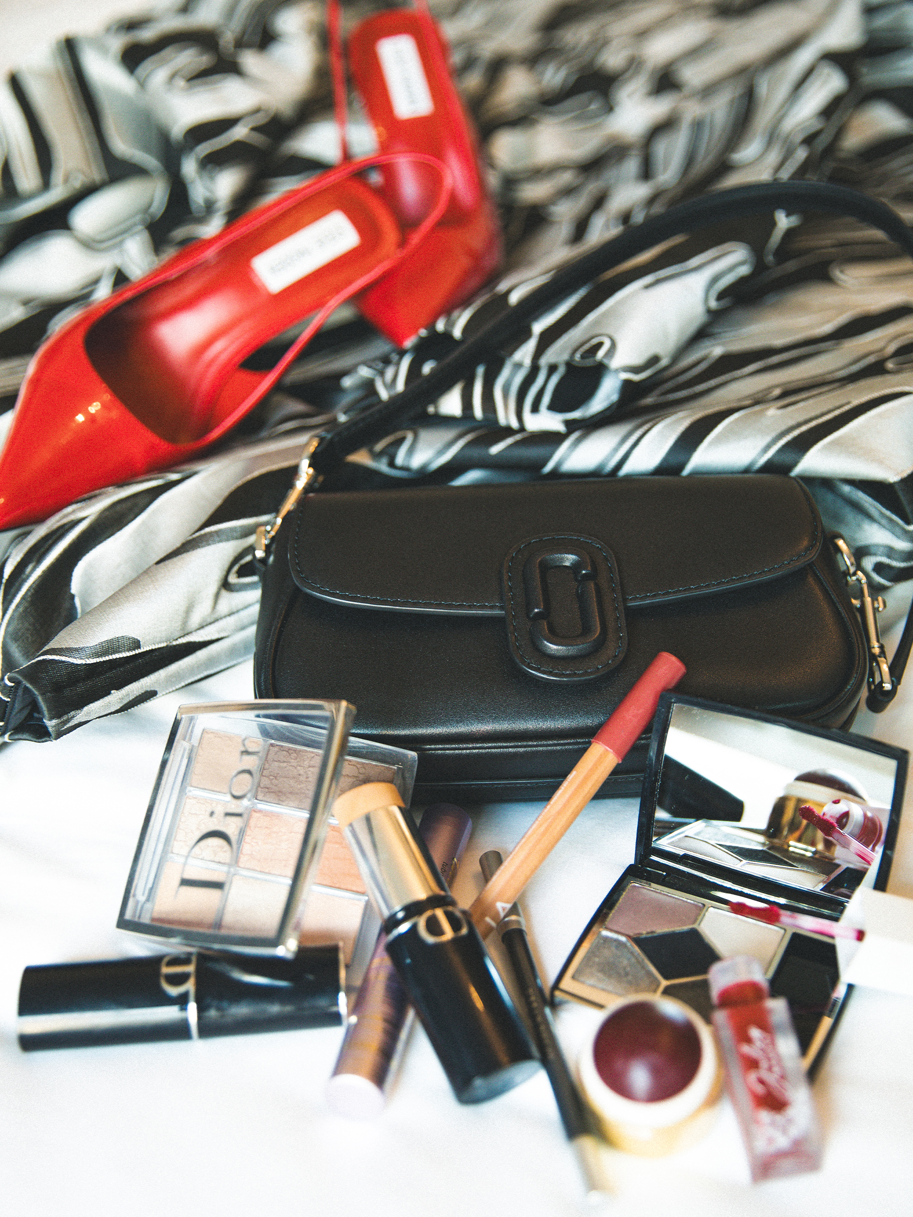 A flat lay photo of Anna Lambe's accessories for the Gotham TV Awards, featuring red slingback heels, a black shoulder bag, and Dior makeup.