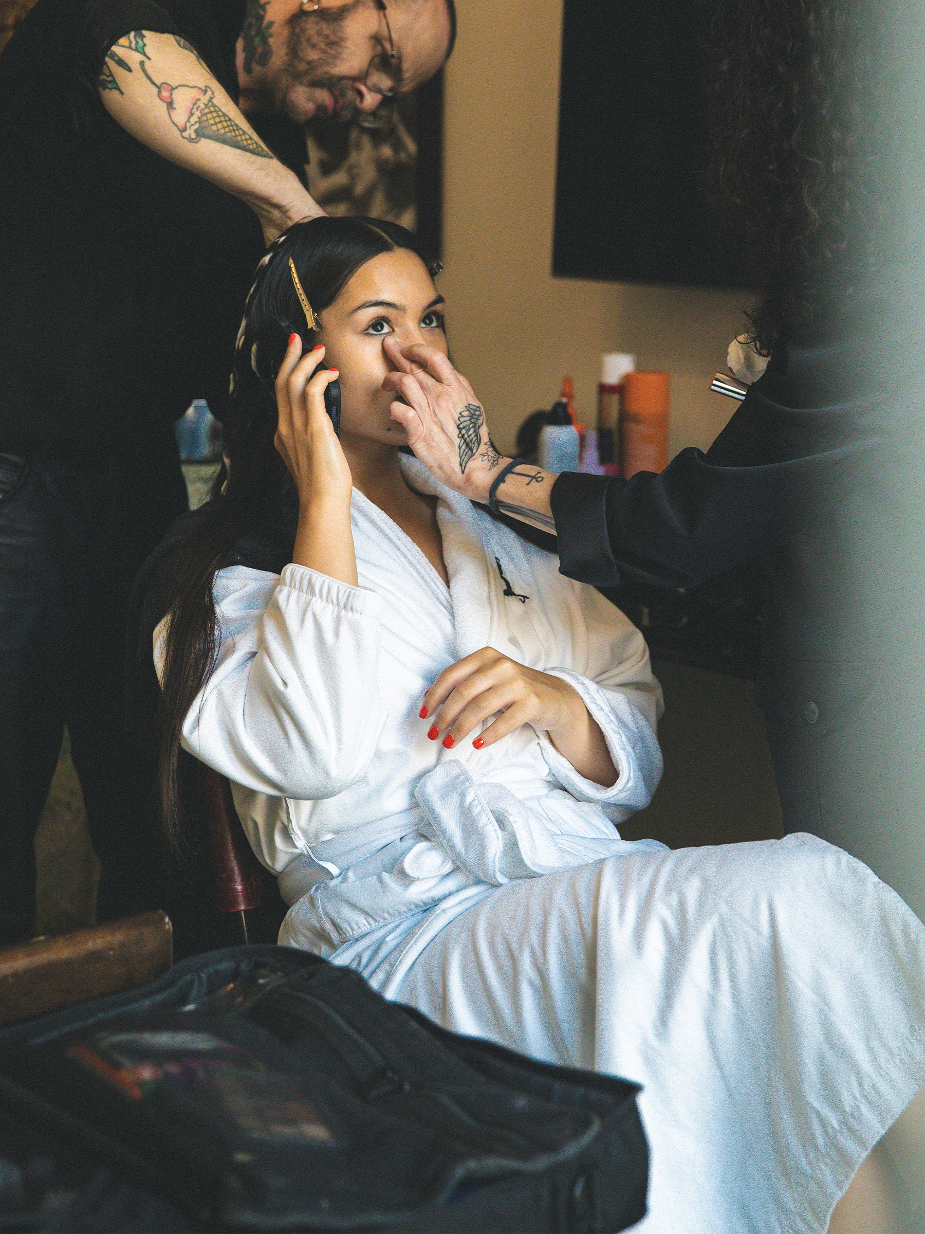 Anna Lambe sitting in the glam chair wearing a white robe and talking on the phone.