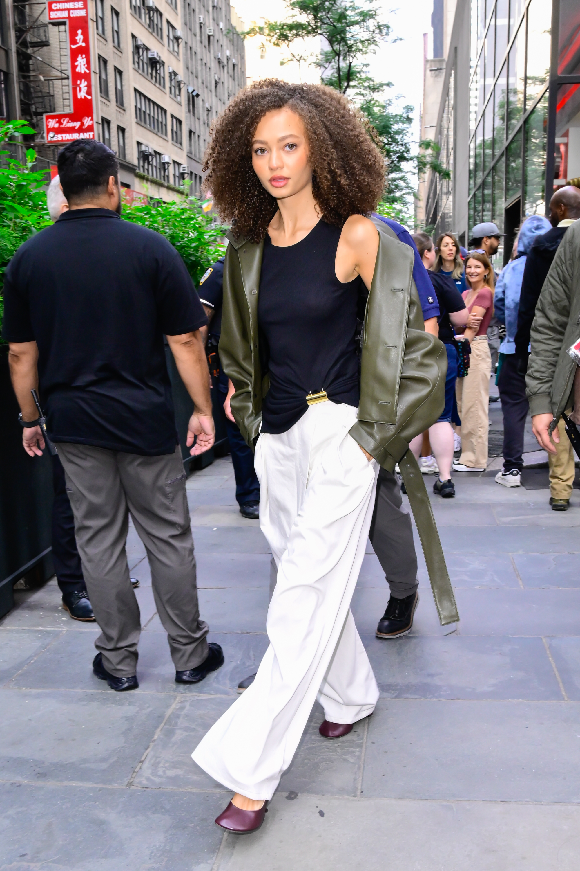 Nicole Parker wearing a black tank top, white pants, and burgundy shoes in NYC