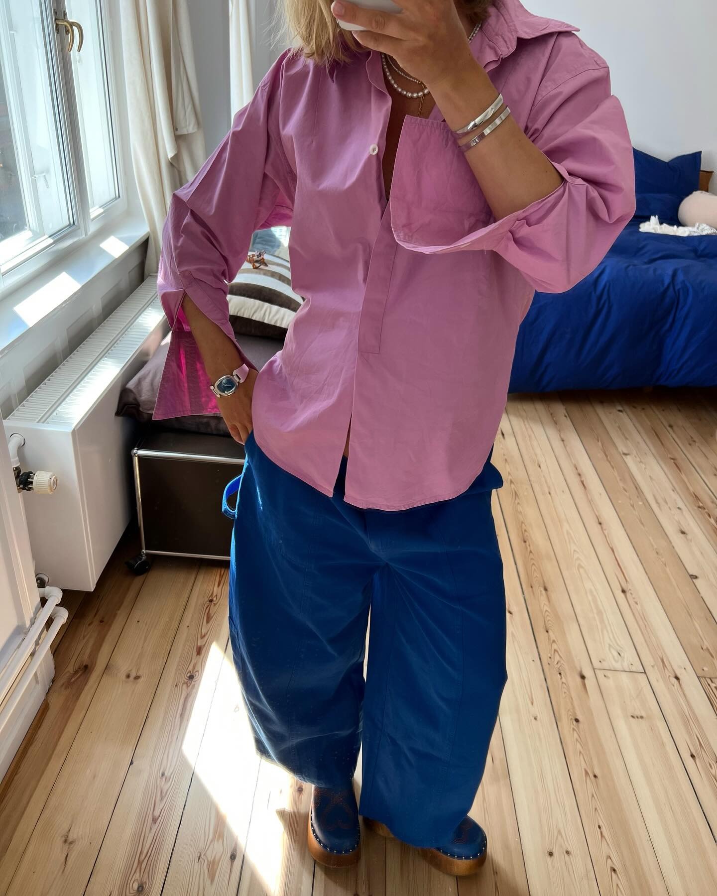 Influencer wears cobalt blue trousers with tonal heeled clogs and a dusty pink shirt.