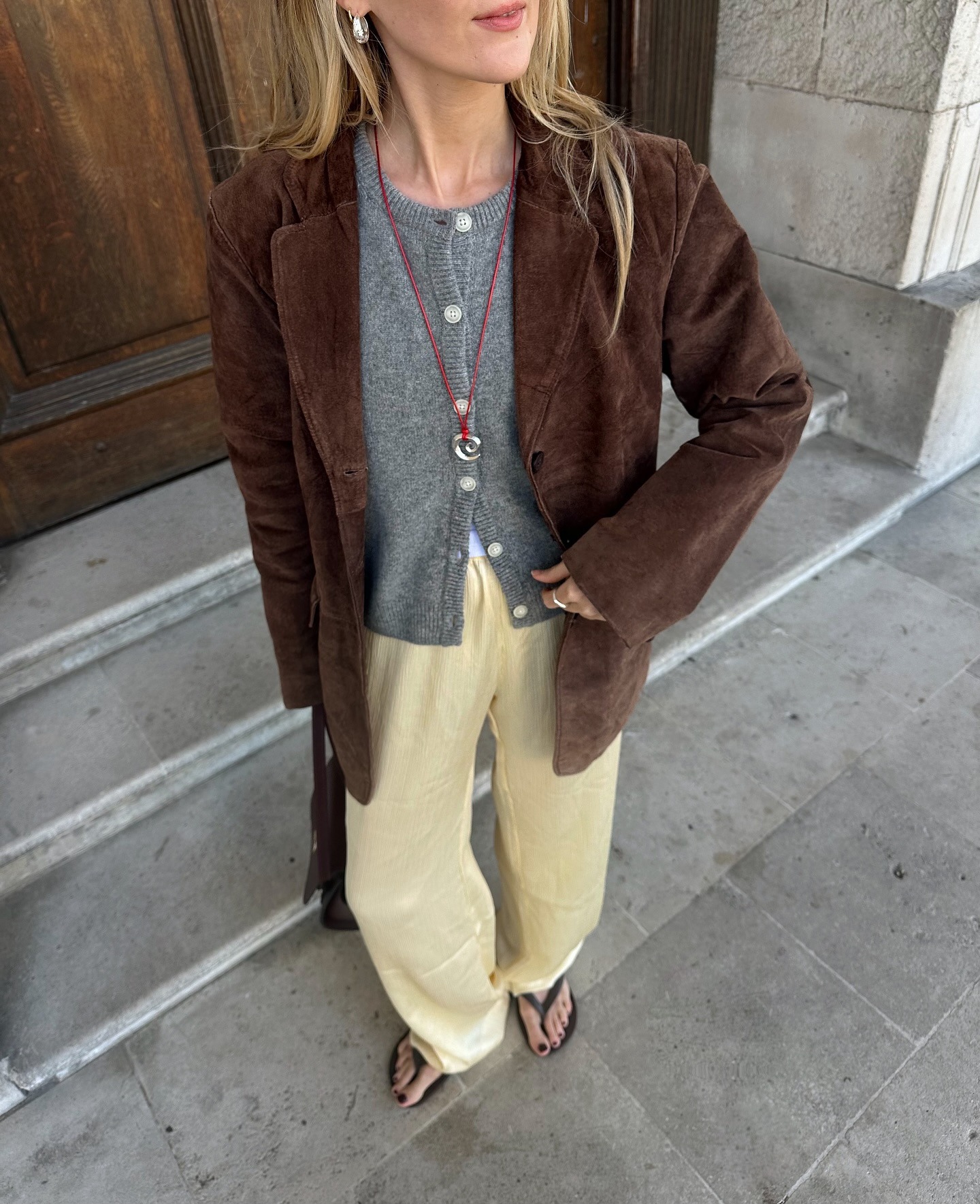Influencer wears butter yellow trousers with a grey cardigan, a brown suede jacket and black leather flip-flops.