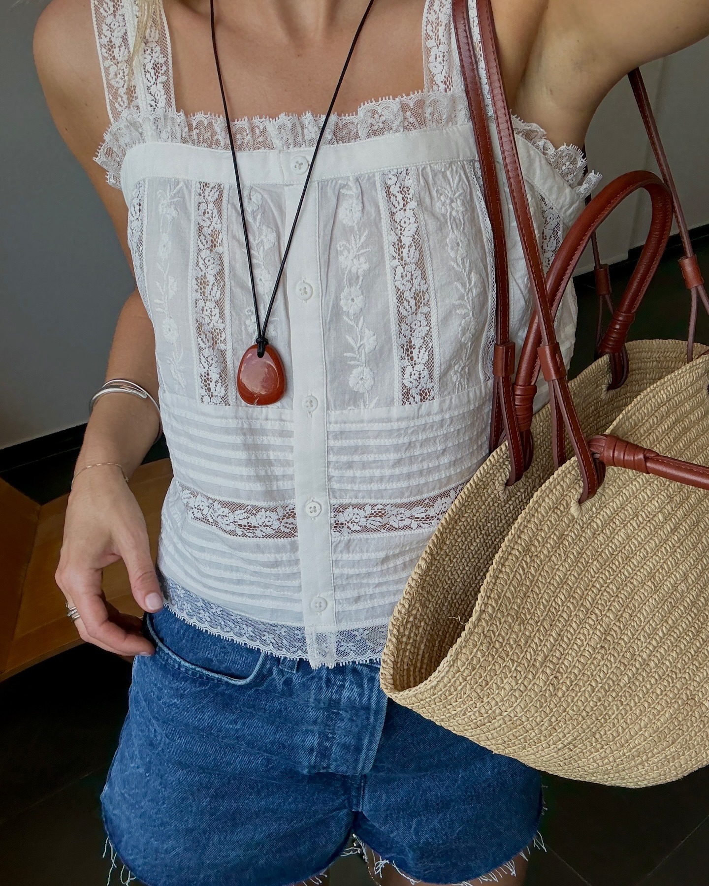 Close-up shot of influencer ﻿@lucywilliams02﻿ wearing a white square-neck blouse from Sezane with cut-off denim, a large basket bag and a long pendant necklace.