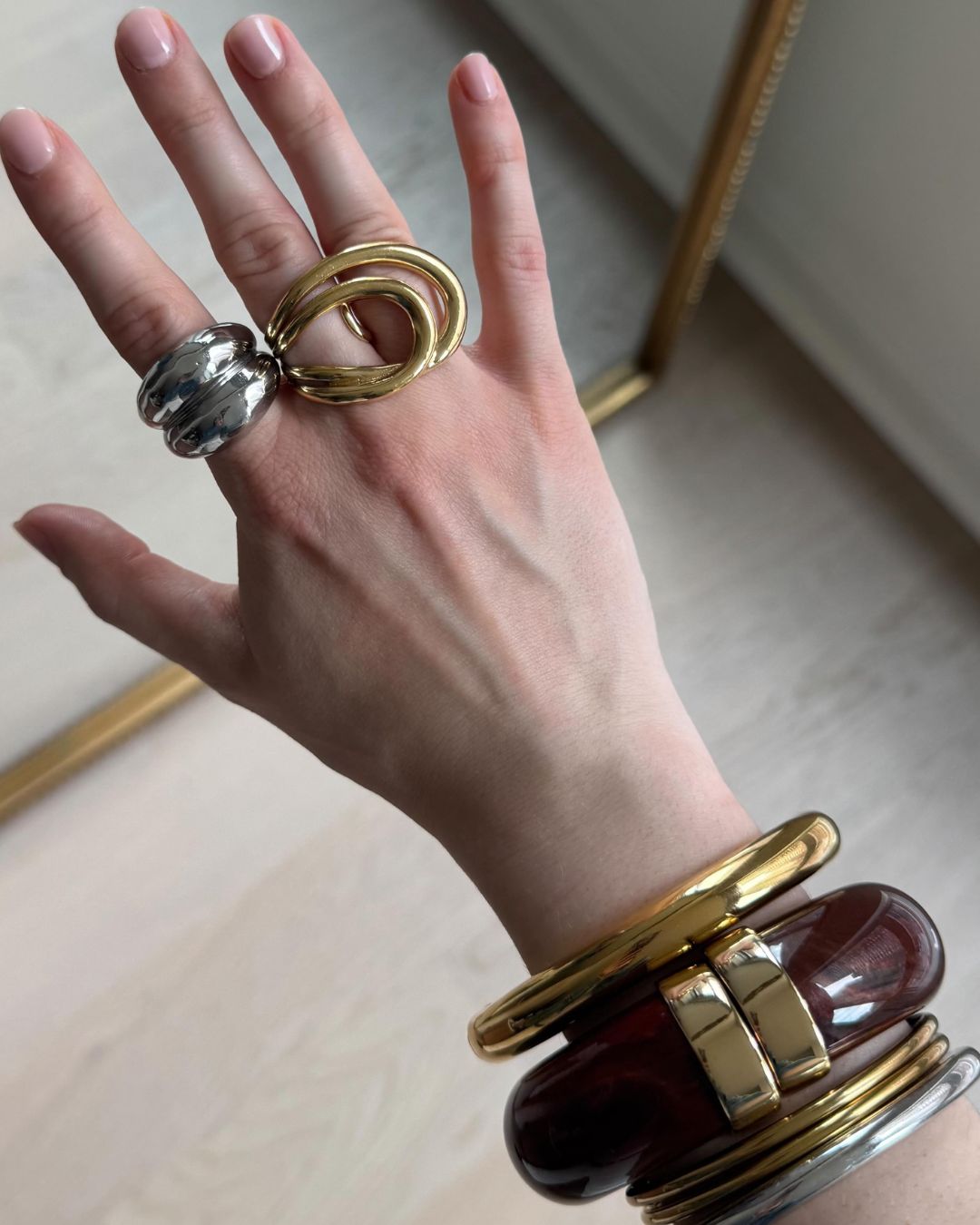 Influencer @trendingwithtinsley shares a shot of her hand, wearing two statement rings on her fingers and multiple bangles in gold, silver and tortoise stacked on her wrist.