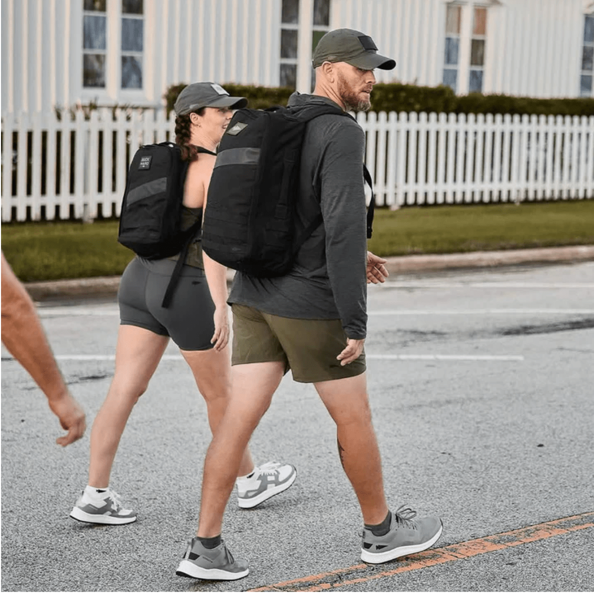 Two people walking down a street wearing backpacks.