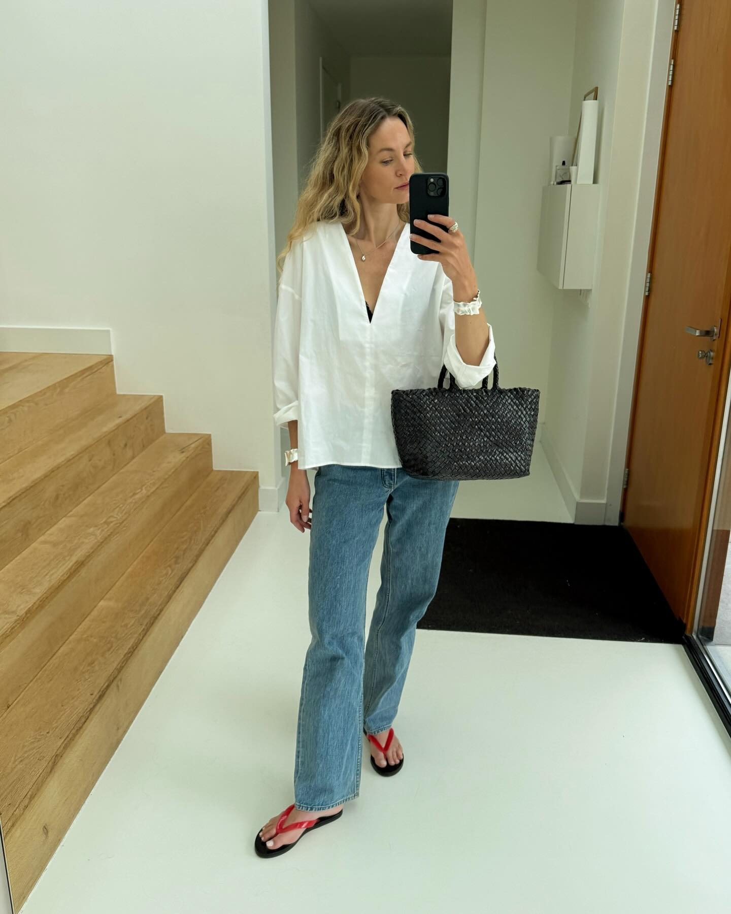 Woman wears white shirt, woven basket bag, blue jeans and red jelly sandals