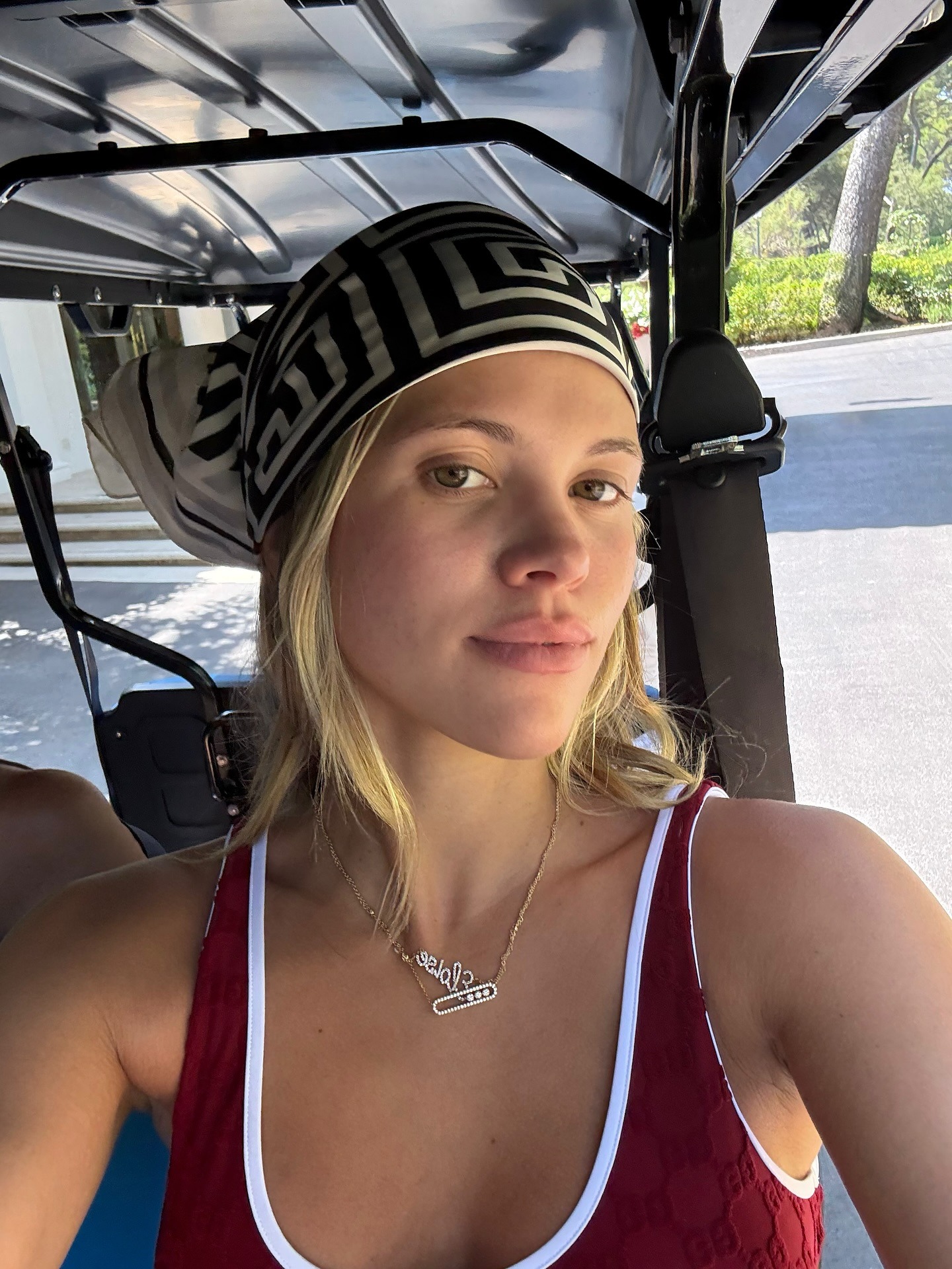 Sofia Richie Grainge in the French Riviera wearing a Gucci burgundy one-piece swimsuit, black pants, red flip flops, a brown Miu Miu bag, and a silk scarf.