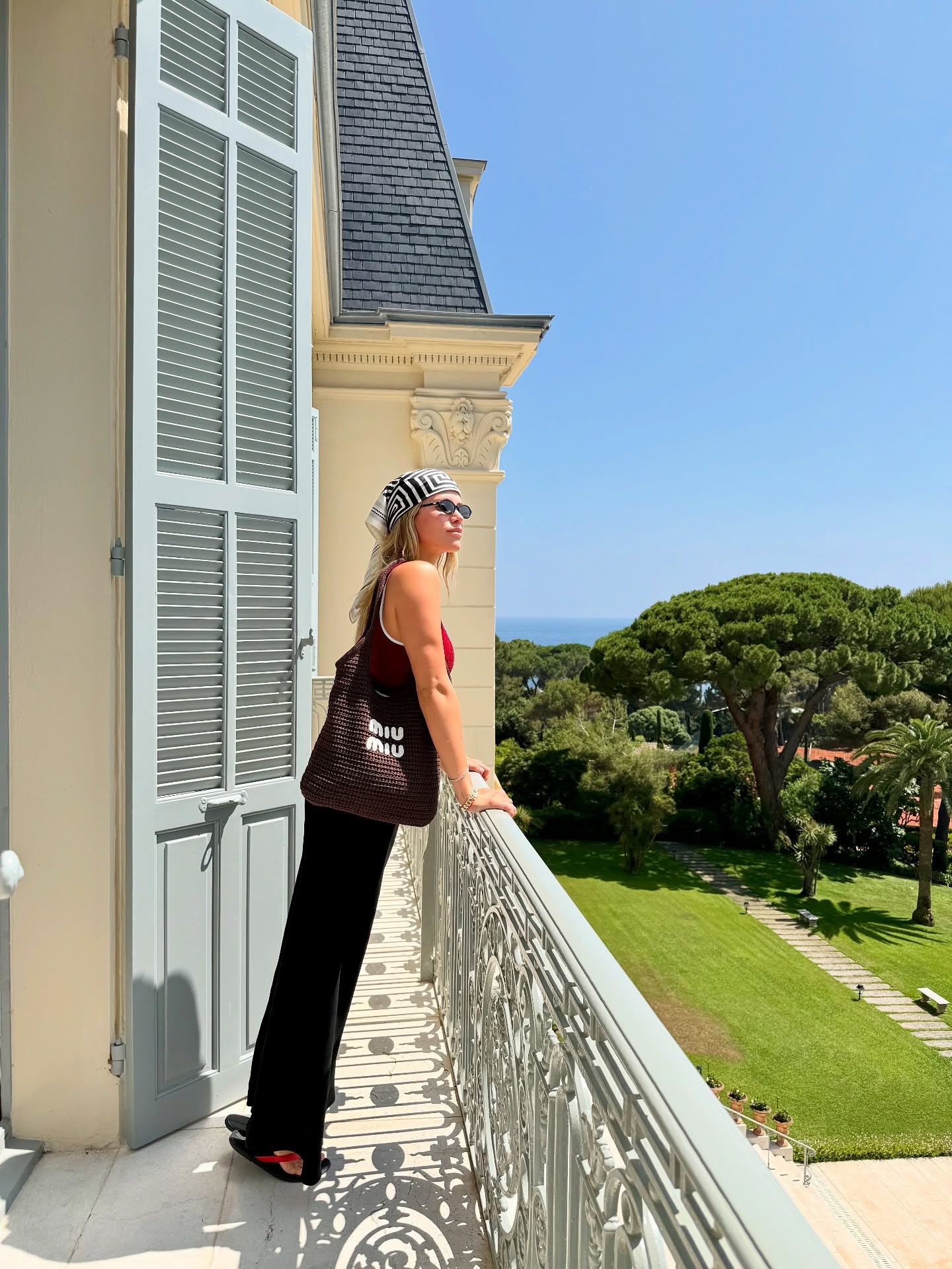Sofia Richie Grainge in the French Riviera wearing a Gucci burgundy one-piece swimsuit, black pants, red flip flops, a brown Miu Miu bag, and a silk scarf.
