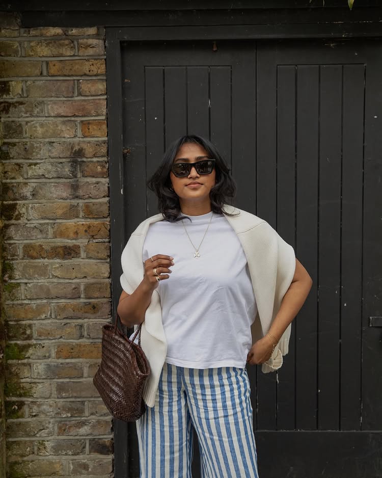@chiarasatelier carries a brown woven leather bag whilst wearing a white T-shirt and blue stripe trousers