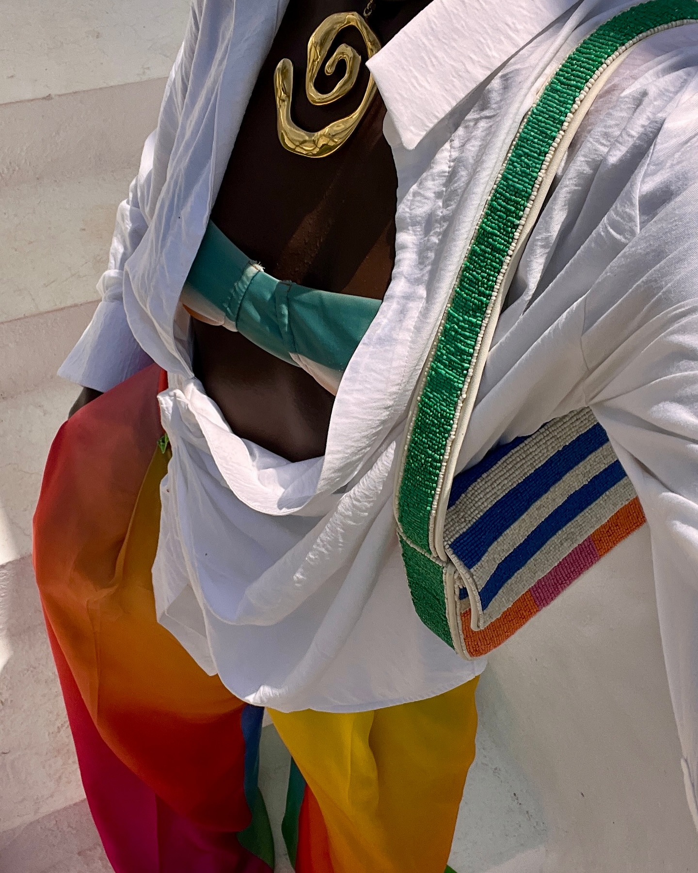 @spiritedpursuit wears a beaded Staud bag with a white shirt and orange ombre trousers