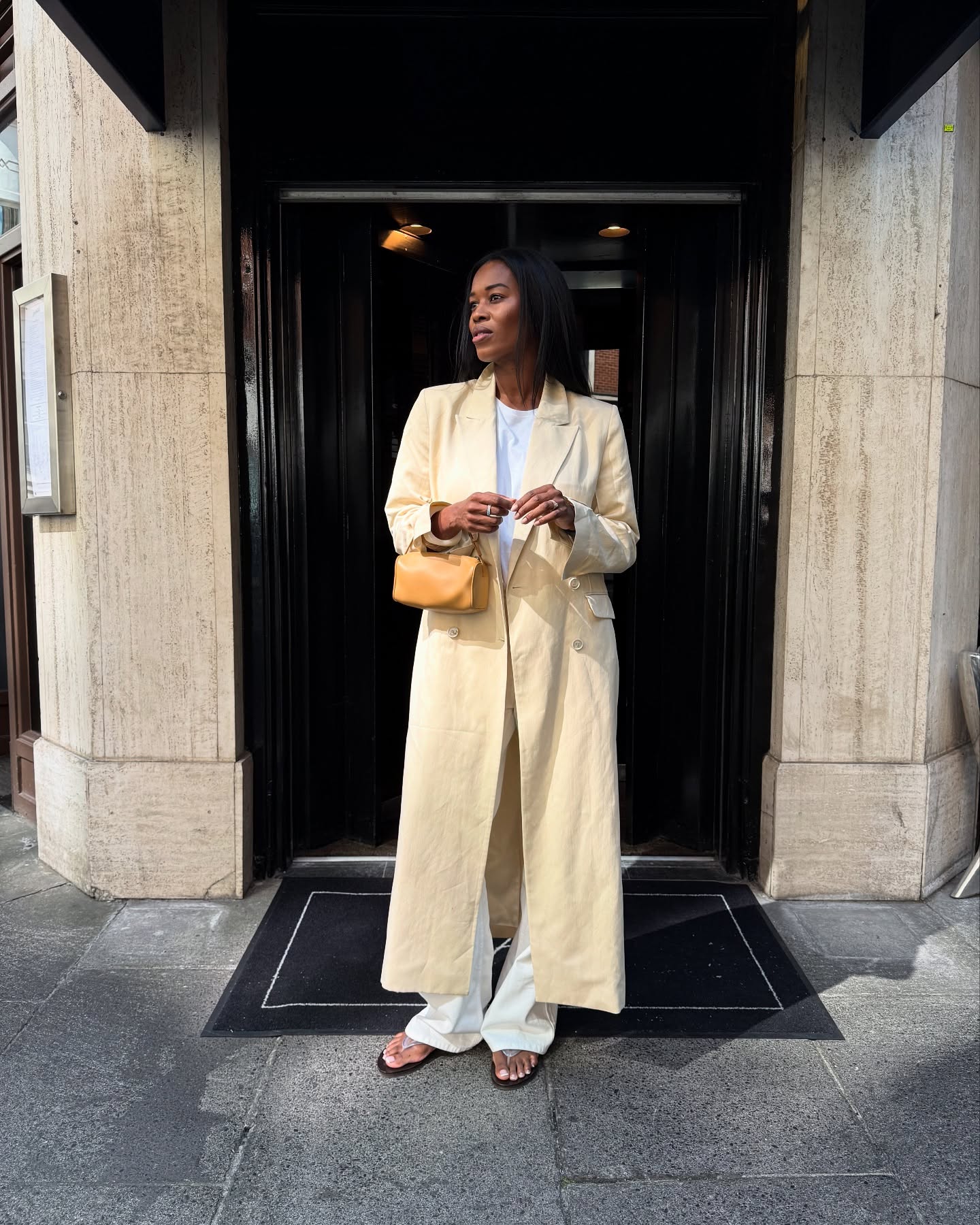 @nlmarilyn wears a cream coat with a tan mini leather bag