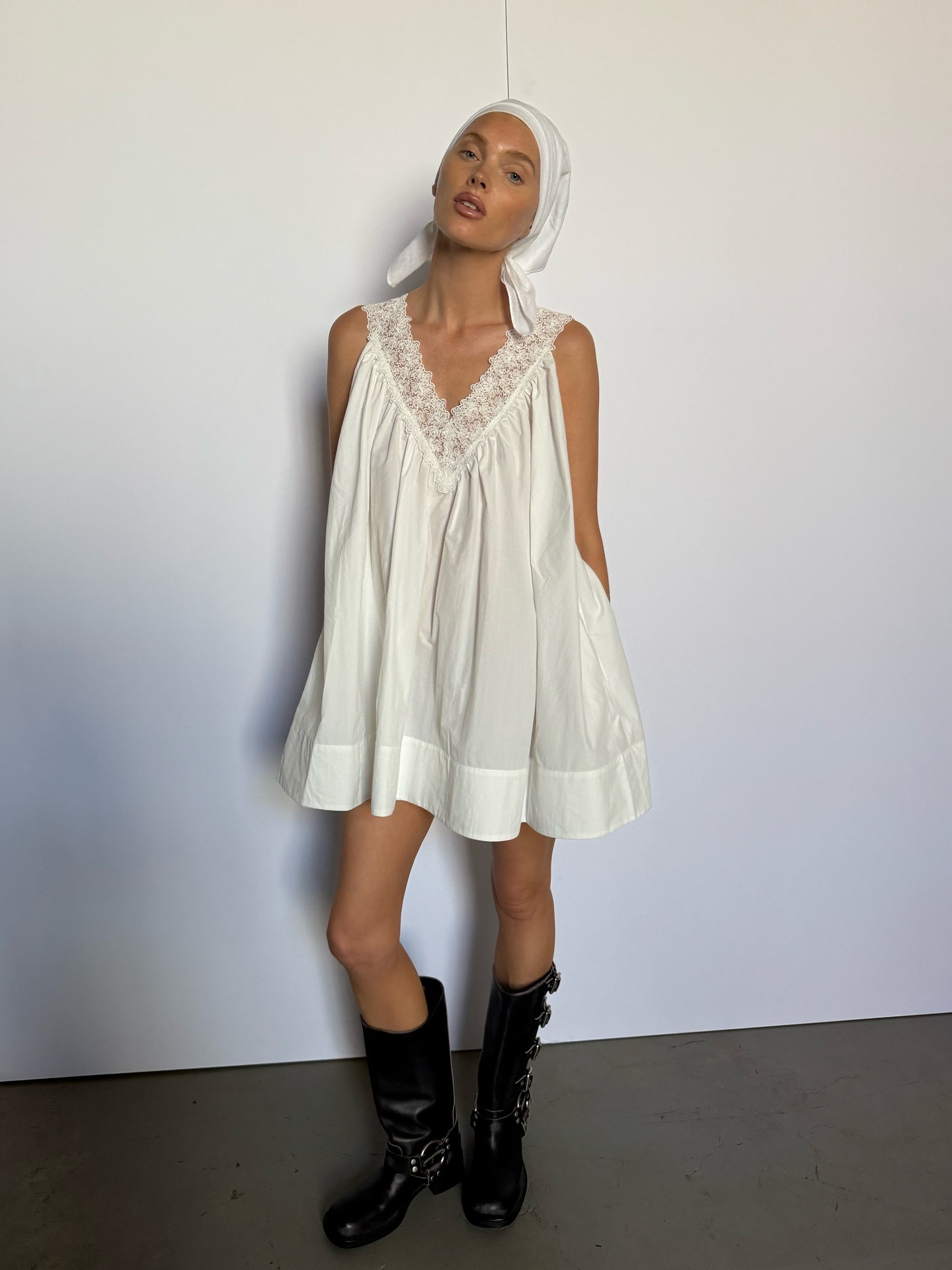 Elsa Hosk wears a white sleeveless minidress with black biker boots and a white headscarf.