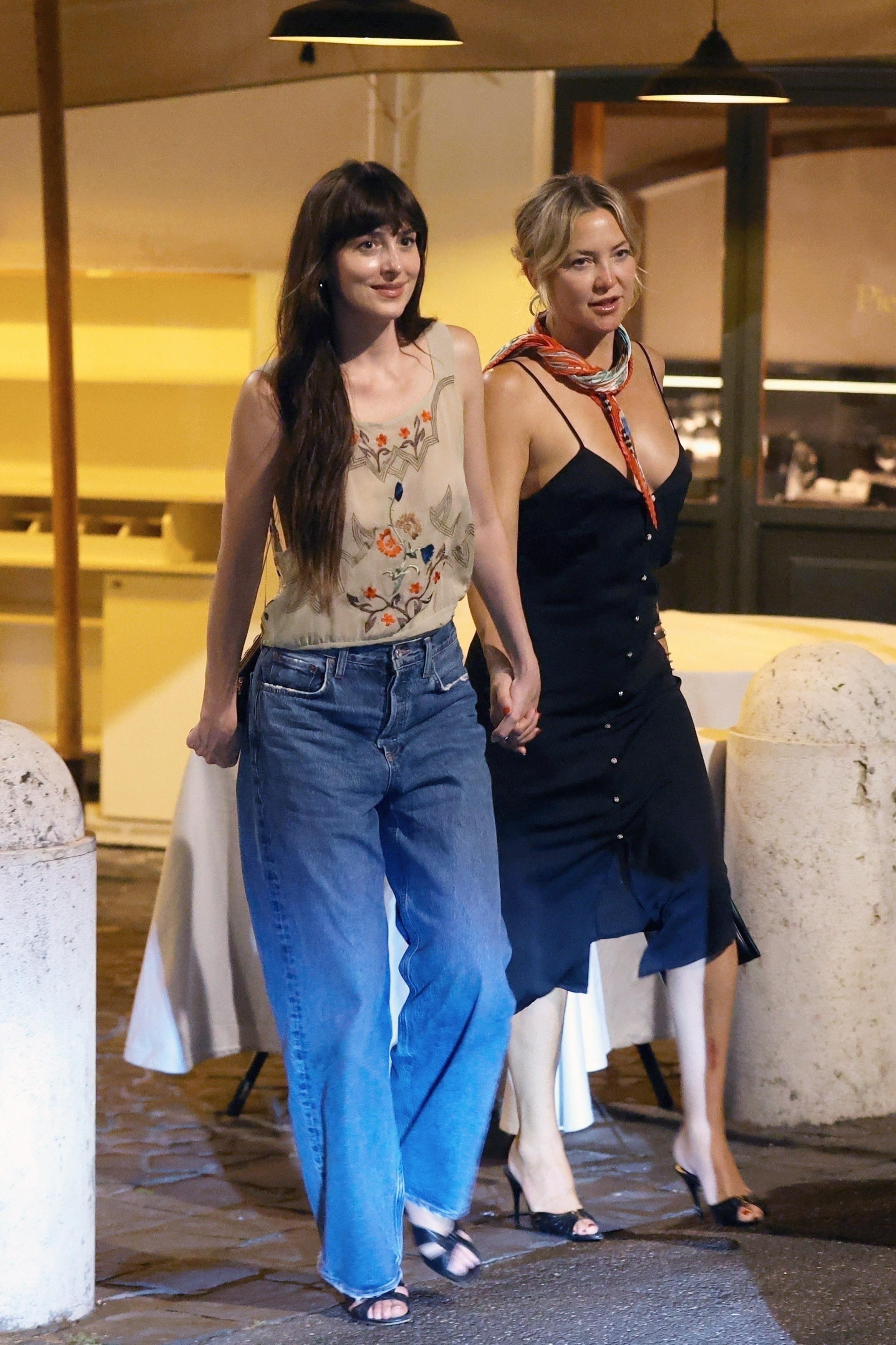 Dakota Johnson steps outside holding hands with Kate Hudson. She wears a vintage style top with baggy jeans and black heeled sandals.