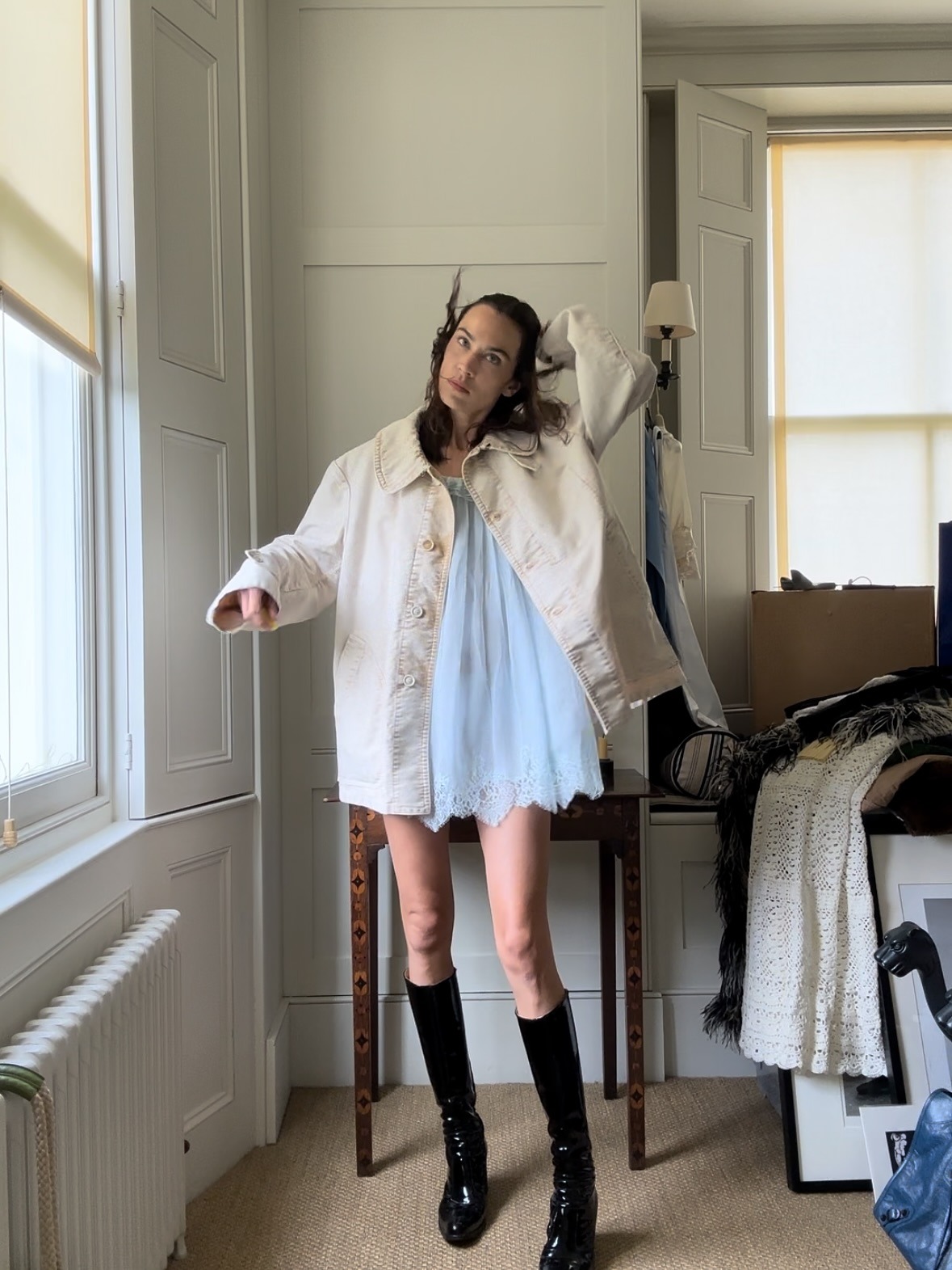 Alexa Chung wears a white cotton minidress with a cream barn jacket and black knee-high heeled boots.