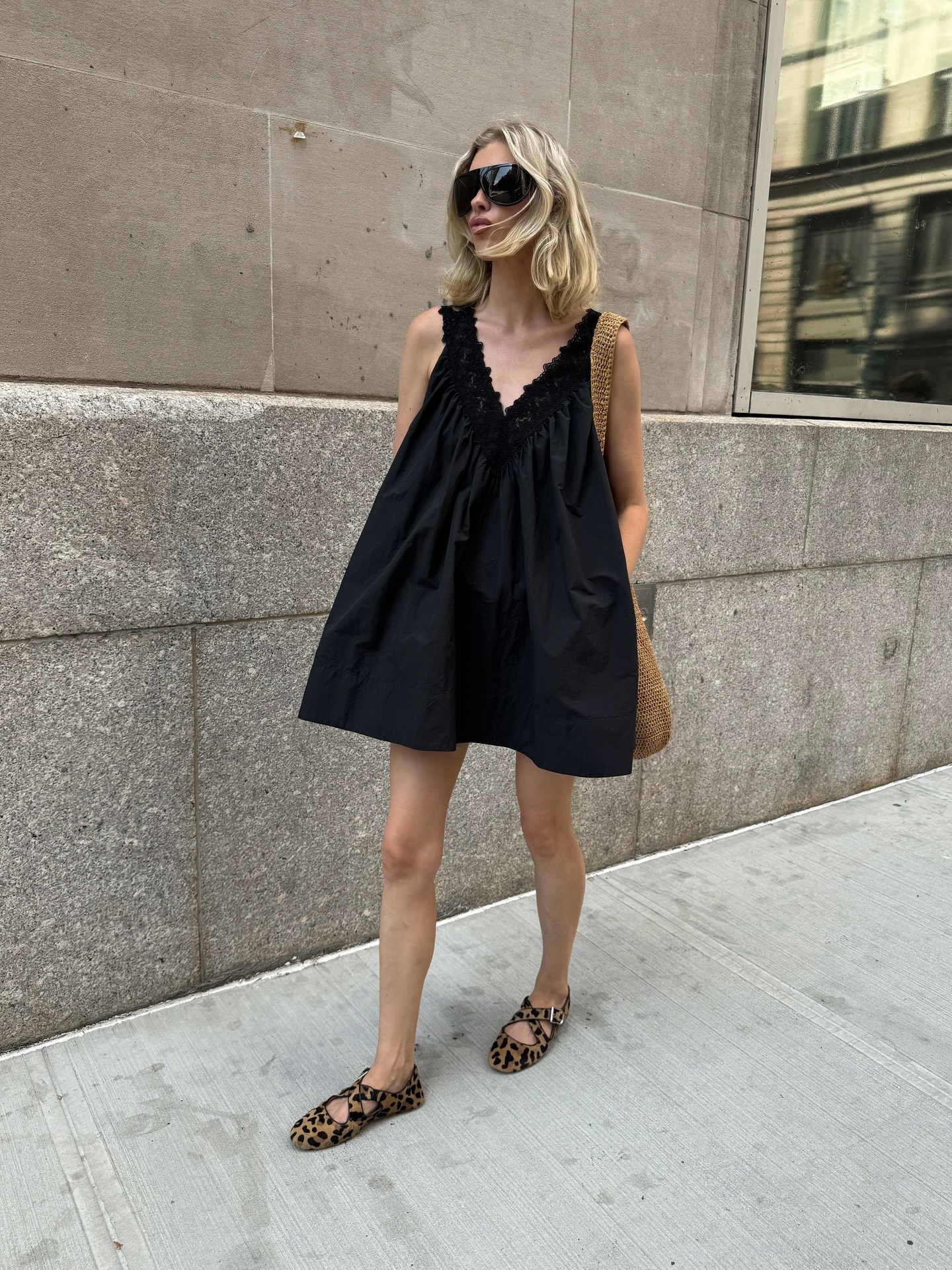 @hoskelsa walks outside wearing a black cotton minidress with leopard print ballet flats and oversized sunglasses.