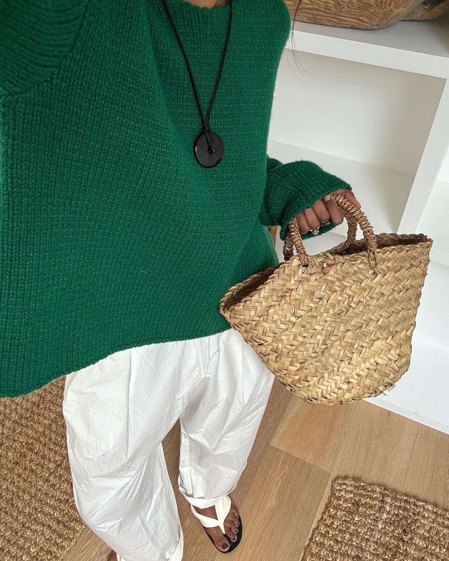 Monikh wears a green sweater, white pants, flip-flops, and a straw tote bag.
