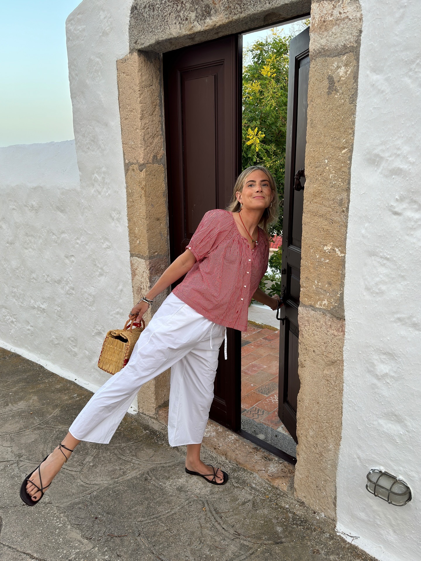 Lucy wears a red blouse, white pants, black sadnals, and a straw bag.