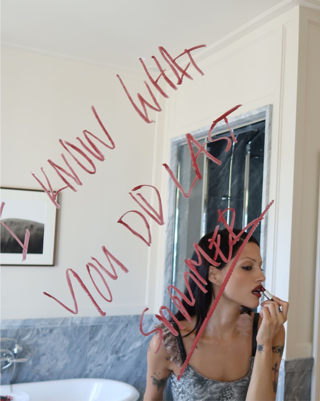 An image of Gabbriette applying her lipstick in the mirror with the words "I Know What You Did Last Summer" written in lipstick.