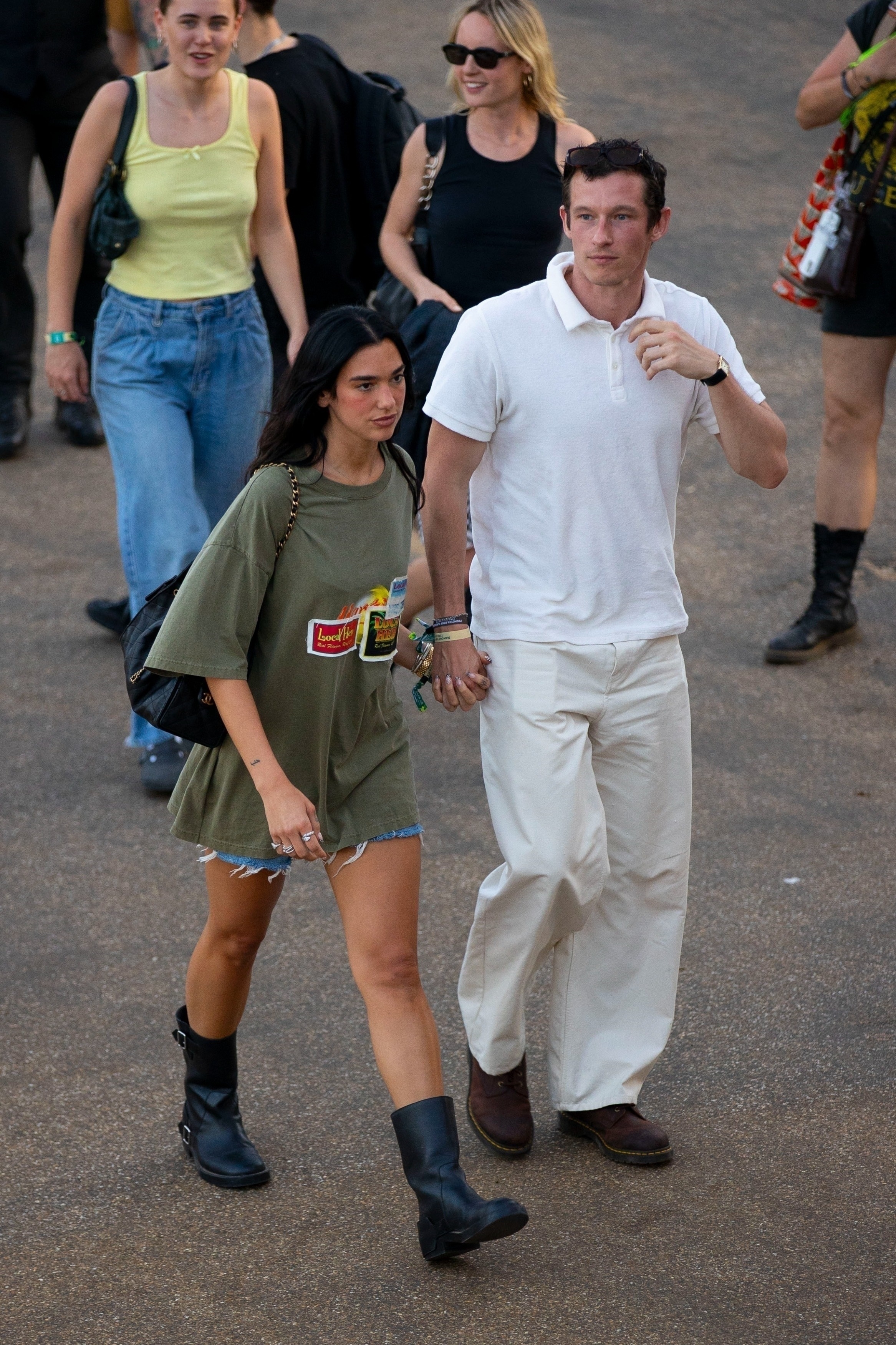 Dua lipa wears an oversize graphic t-shirt, denim shorts, a black chanel bag, and black moto boots.