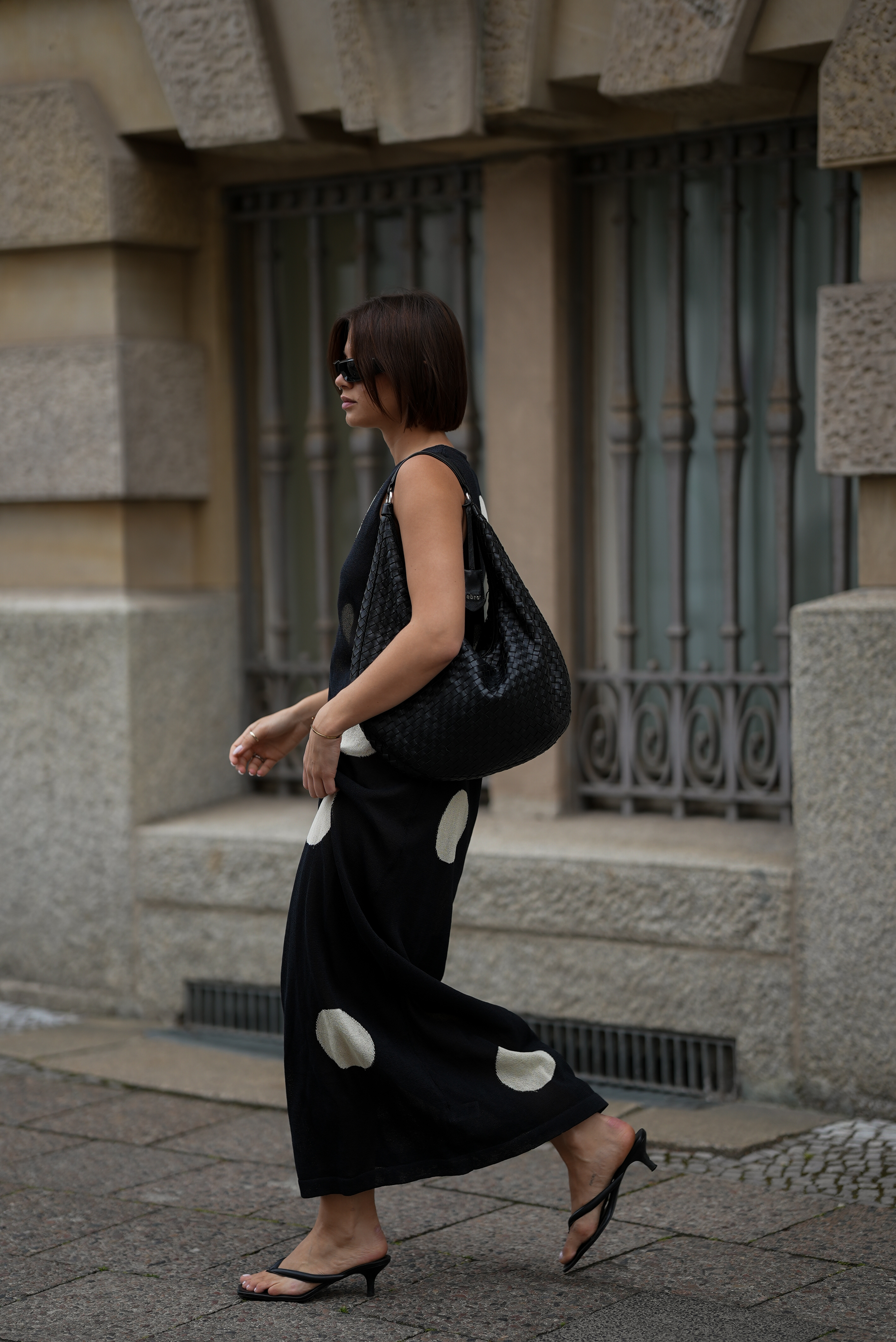 A woman wears a polka dot dress with black kitten heel flip flops.