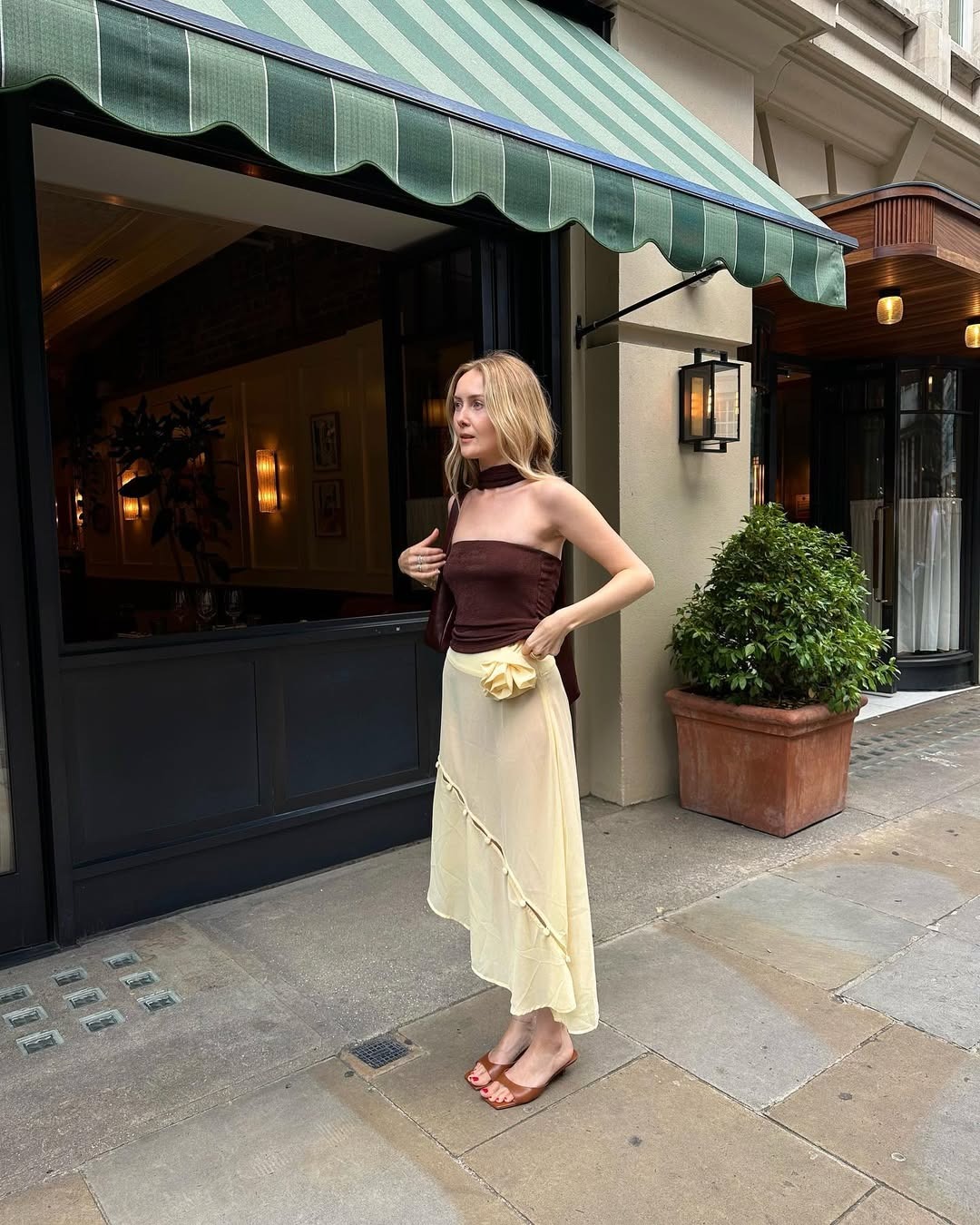 Influencer Chloe Kath Butler wears a butter yellow sheer skirt, a brown tube top, and brown kitten heel sandals.