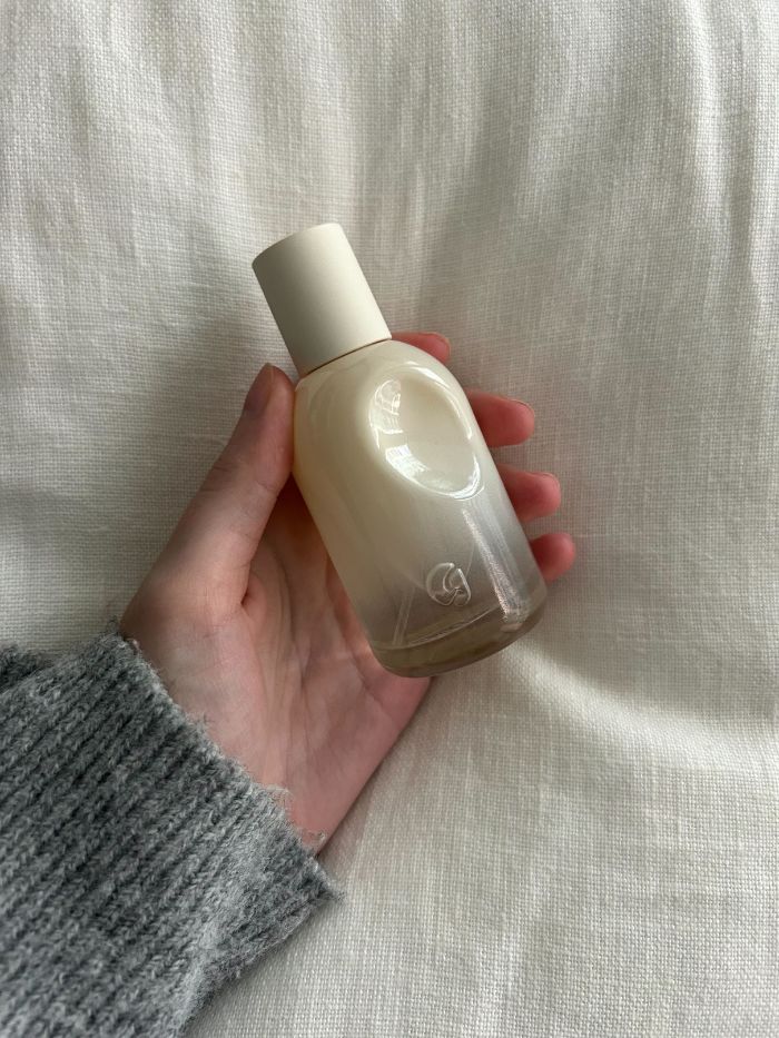 Junior beauty editor holding the Glossier You Doux perfume on a white linen background