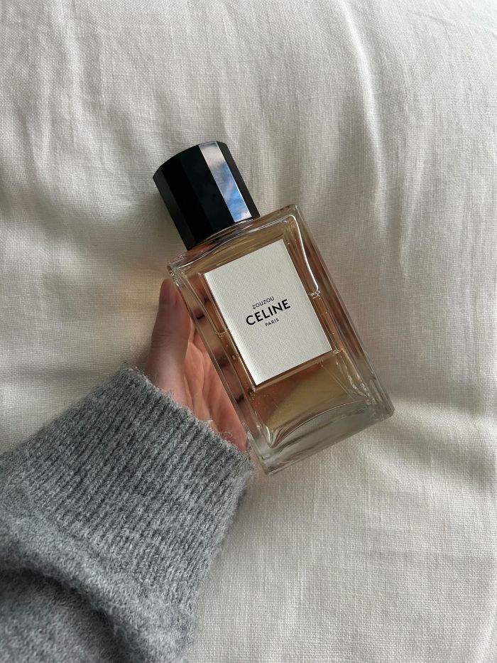 Junior beauty editor holding the Celine Zouzou perfume on a white linen background