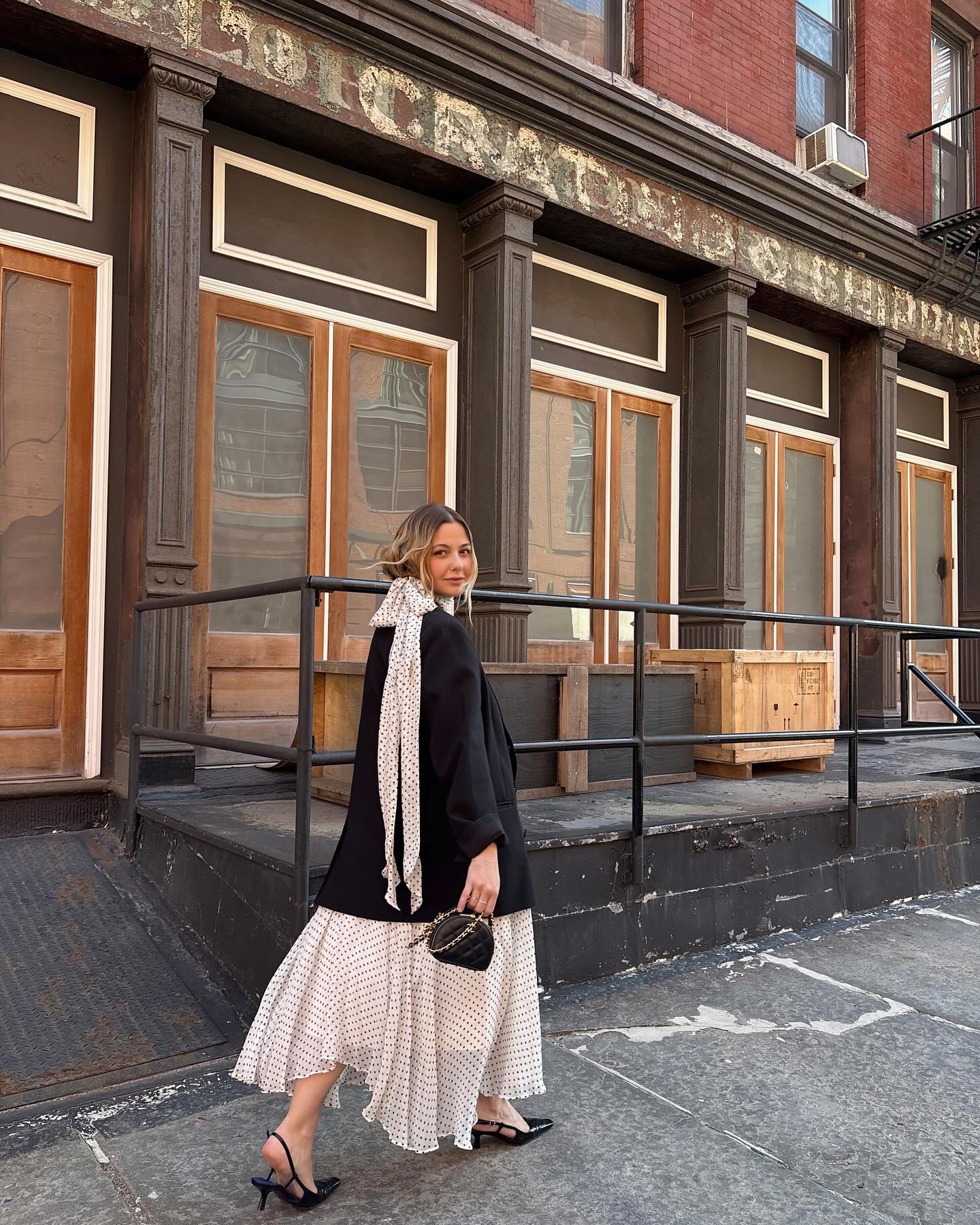 Influencer @oliviamarcus wears a flowy polka dot dress with pointed toe heels and a black blazer.