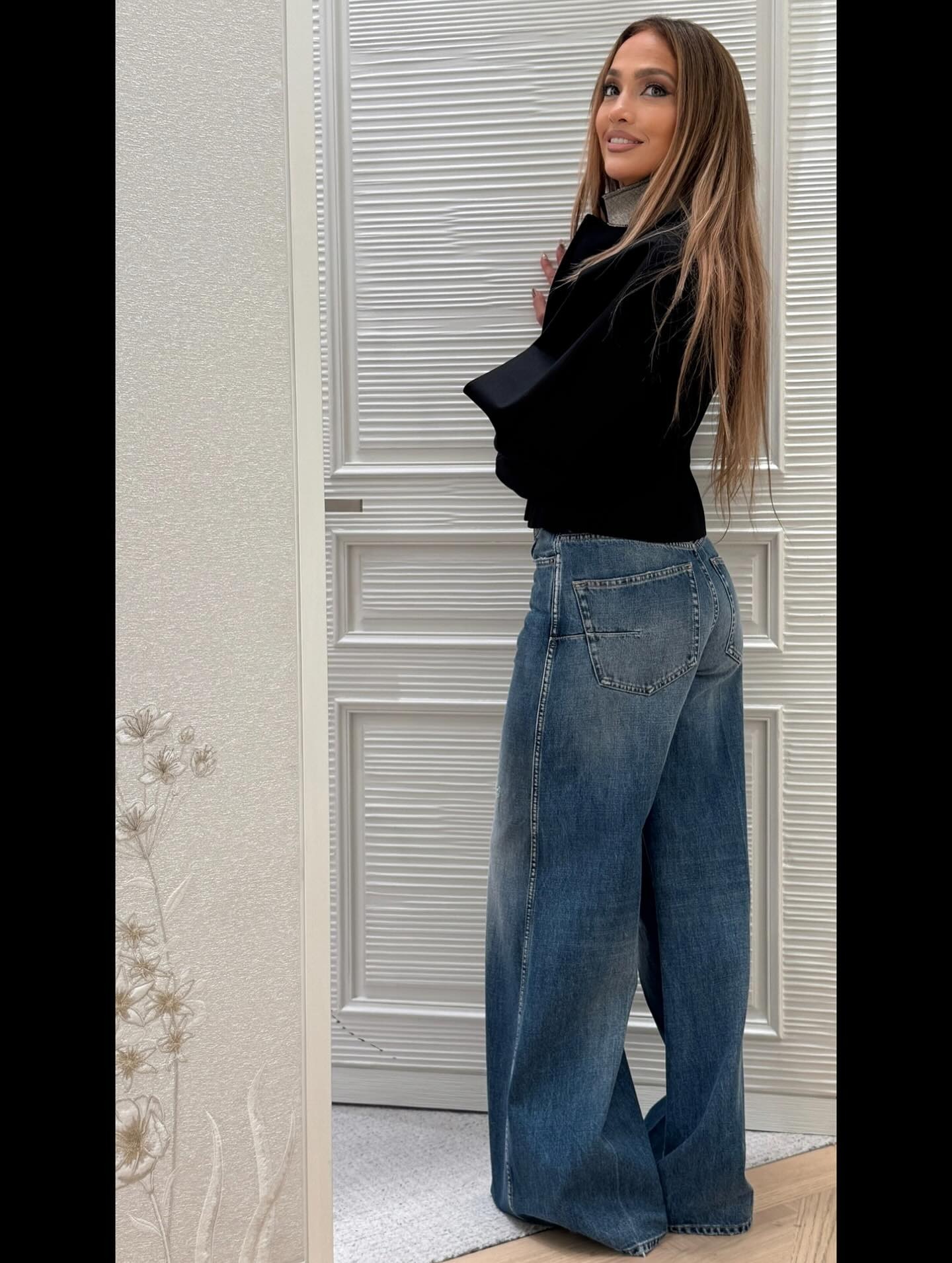 Jennifer Lopez wears dark blue, floor-grazing wide-leg trousers with a black top.