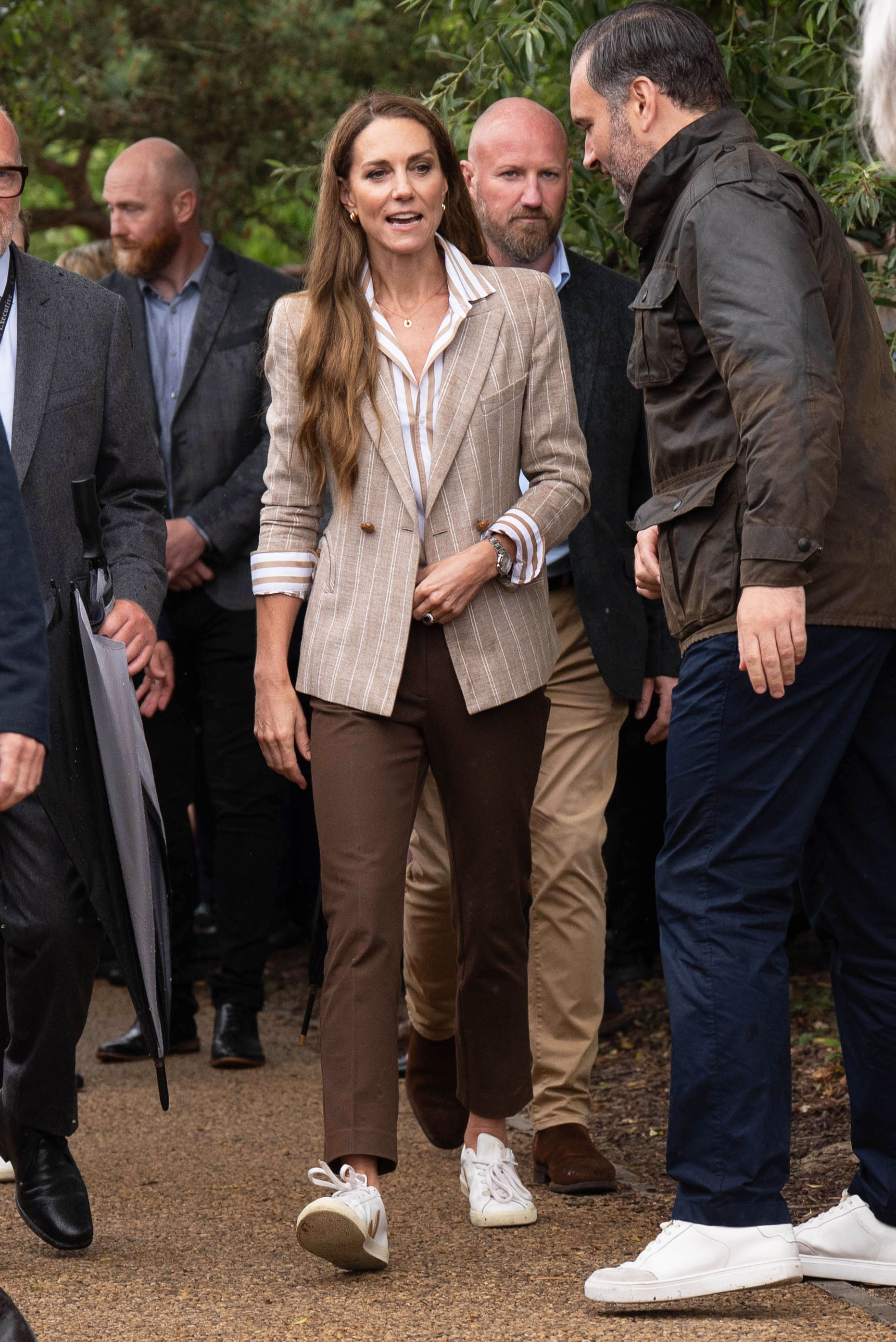 Kate Middleton wears a brown striped blazer with brown pants and white sneakers