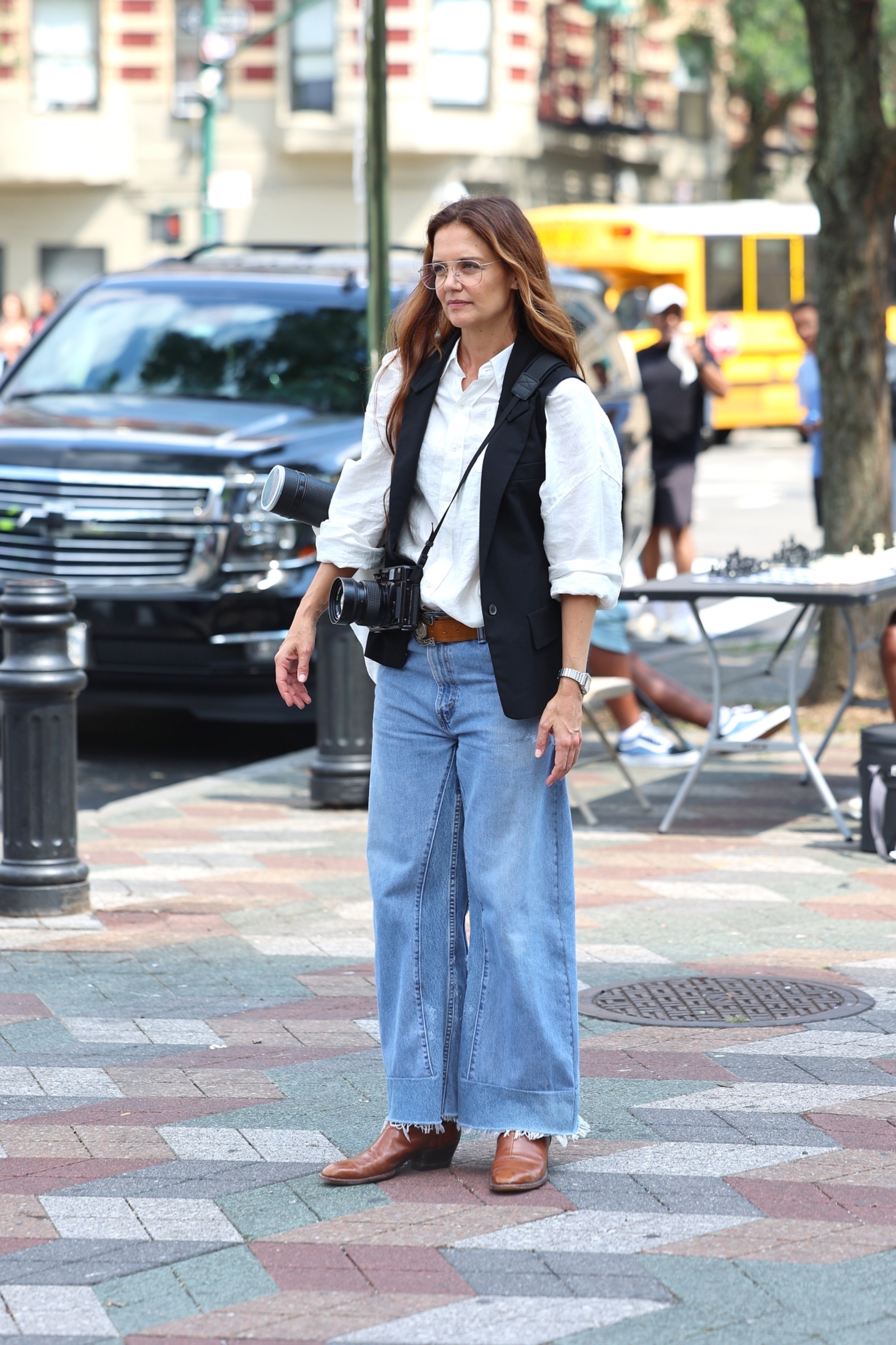 Katie holmes wears a white blouse, black vest, wide-leg jeans, and brown boots.