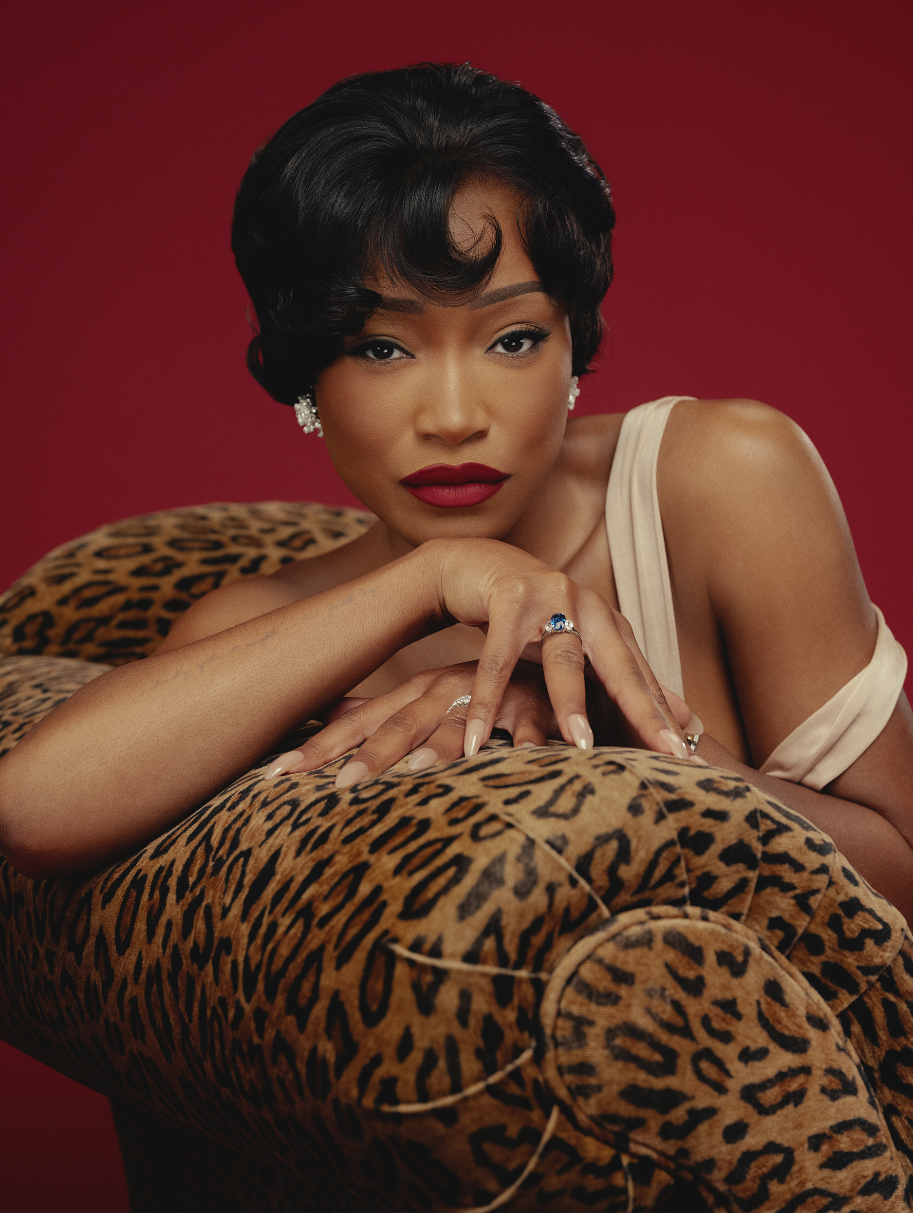 Keke Palmer references Eartha Kitt for Who What Wear's July cover story. She is sitting on a leopard-print couch in front of a red backdrop wearing an off-the-shoulder champagne gown.