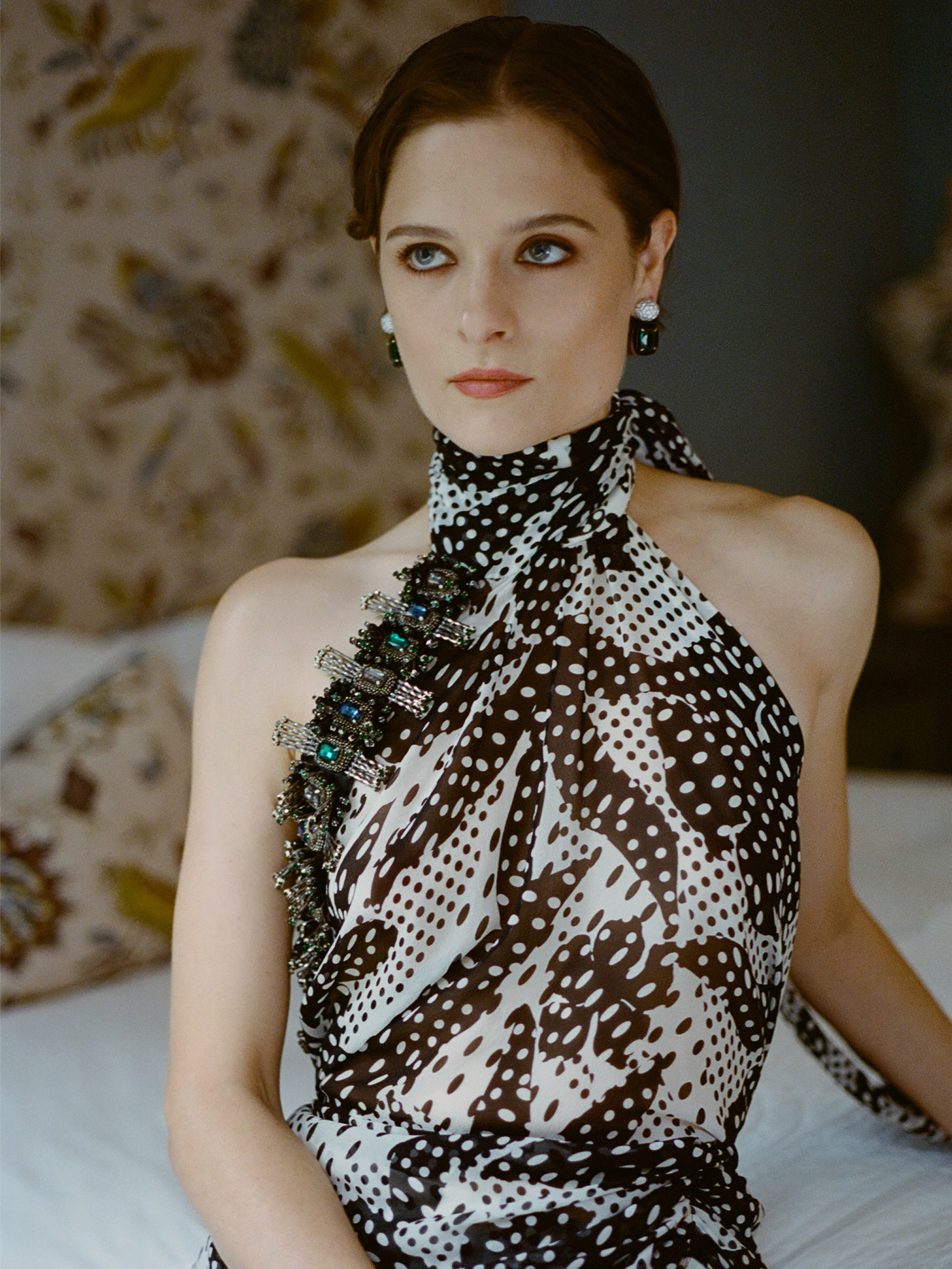 Actress Louisa Jacobson wears a scarf-print Dries Van Noten halter dress with Sauer jewels. She is posing for portraits inside her hotel room before The Gilded Age season 3 premiere.