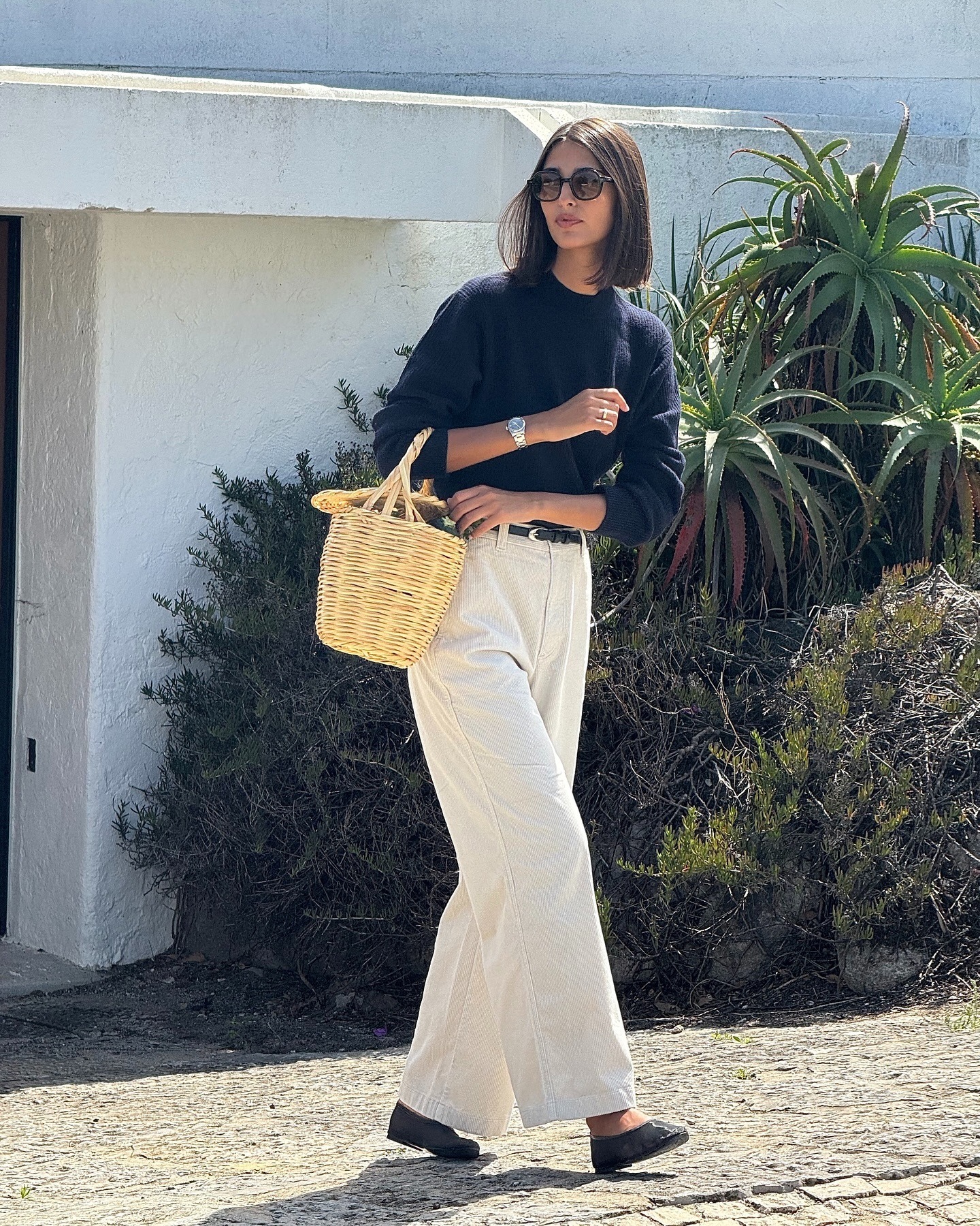 Influencer @salome.mory stands outside wearing a navy jumper with white trousers and black sandals.