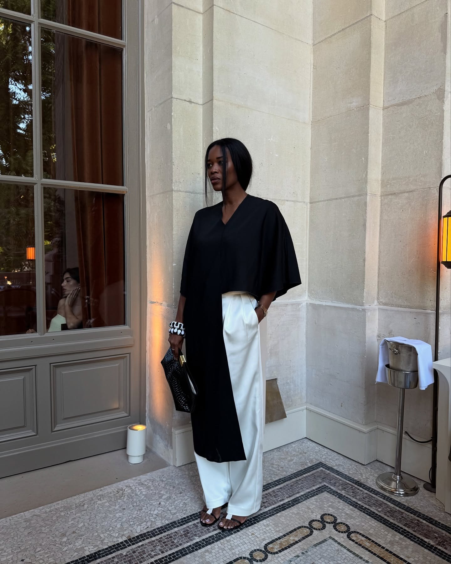 Influencer @nlmarilyn wears a black flowing top with white trousers and black sandals.