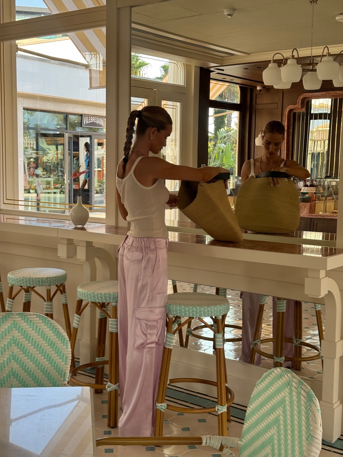 Rosie wears a white tank top, pink silk cargo trousers, and a raffia tote bag.