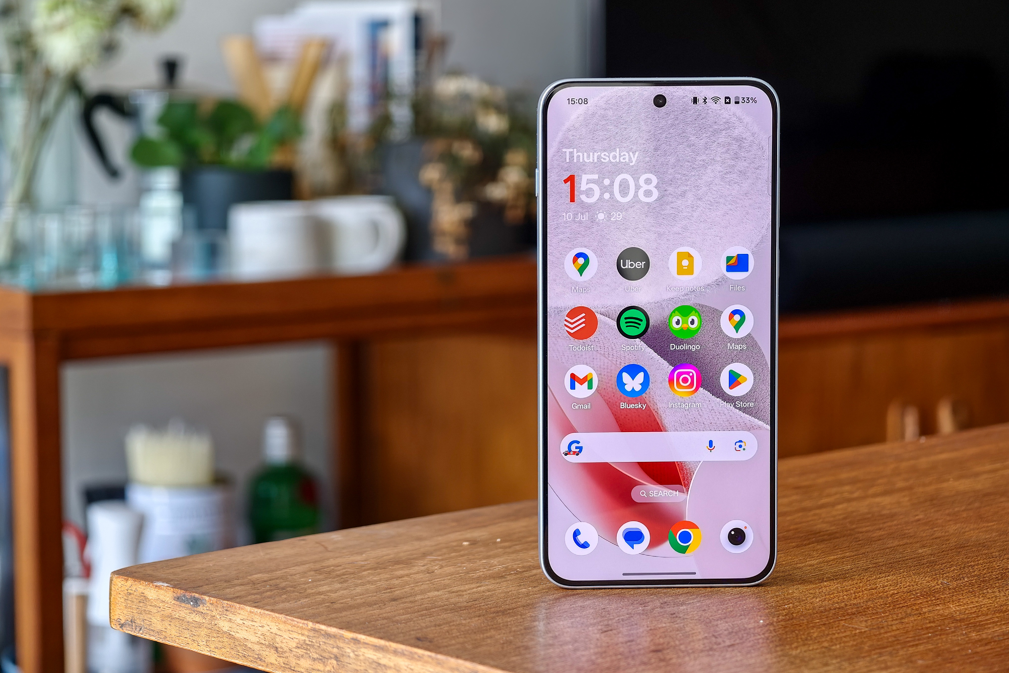 Photo of the OnePlus Nord 5 on a wooden table, with the home screen in view