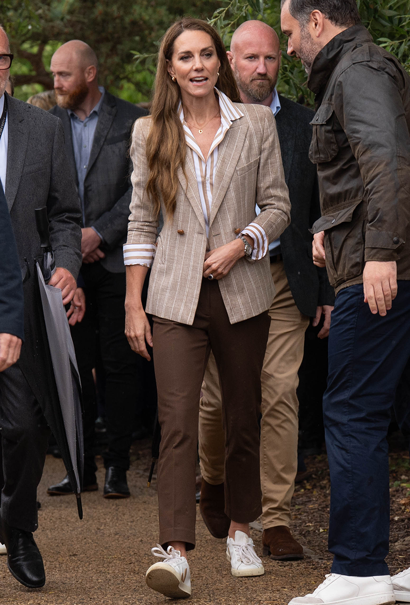 Kate Middleton wearing brown pants with a pinstripe blazer and white sneakers