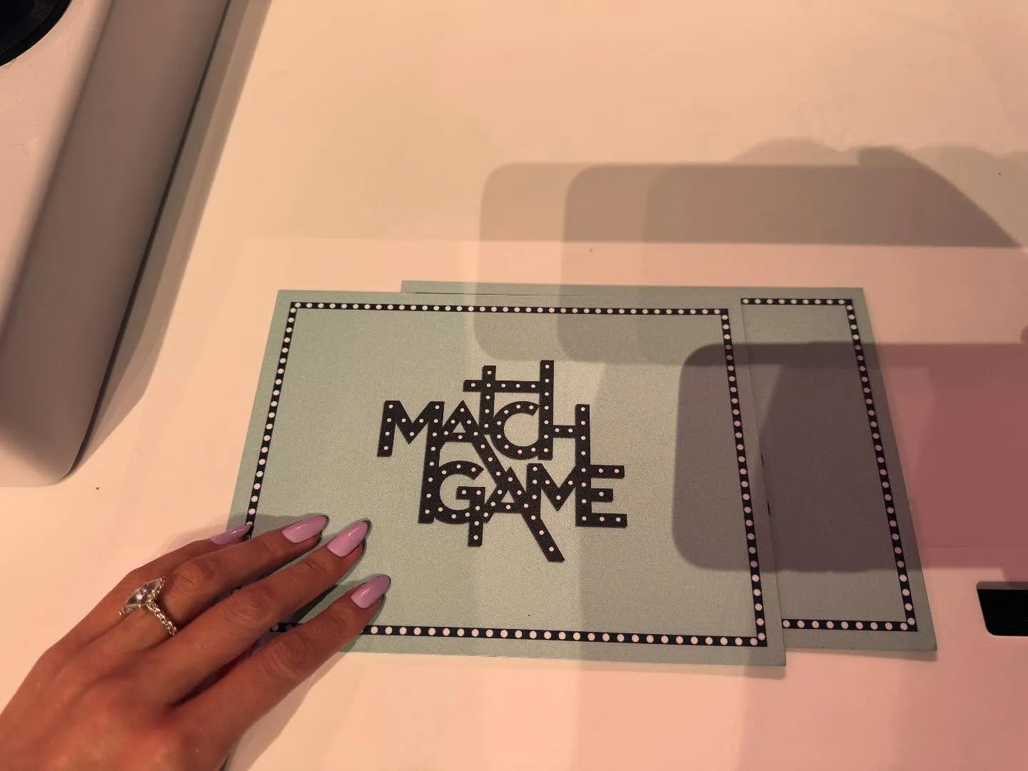 An image from Selena Gomez's Instagram of her hand with lilac nail polish touching a Match Game flashcard.